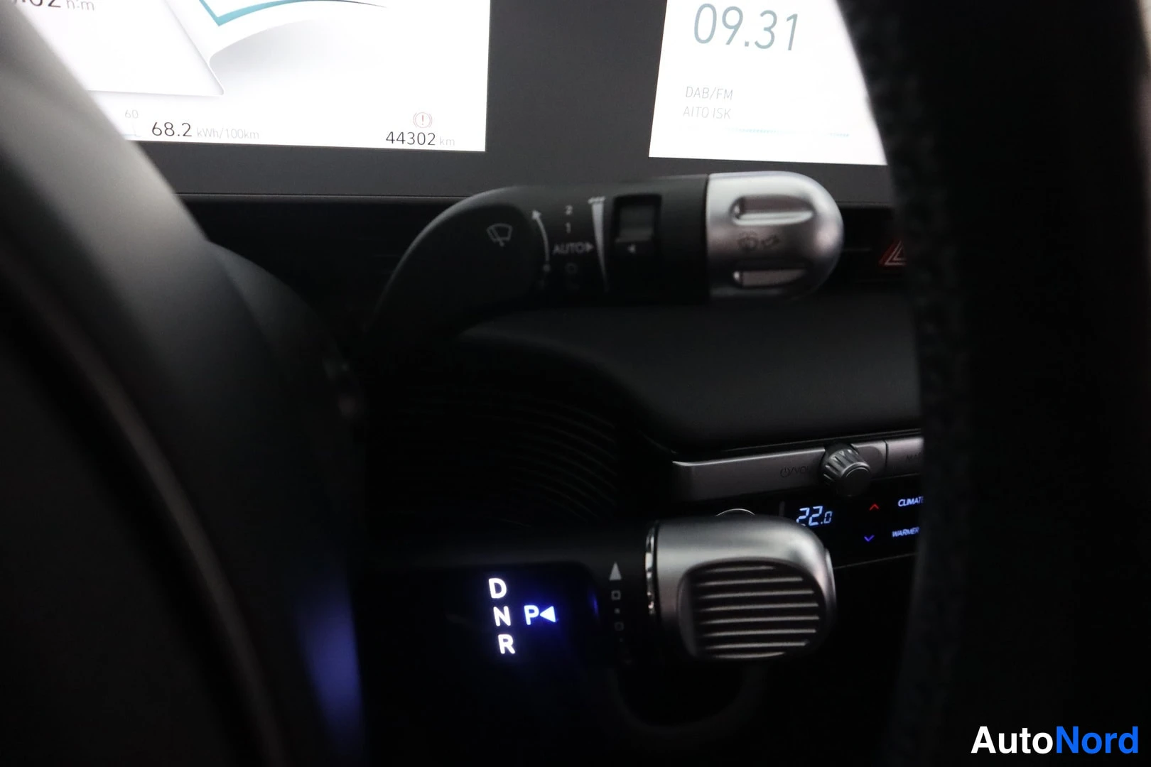 Yksityiskohta: Kojelaudan näytöt: aika 44302 km kertymä, 68.2 kW/h/100km, ilmastointi 22.0 astetta; käyttöpalkki palkilla P-valinnassa, DNR-merkinnät