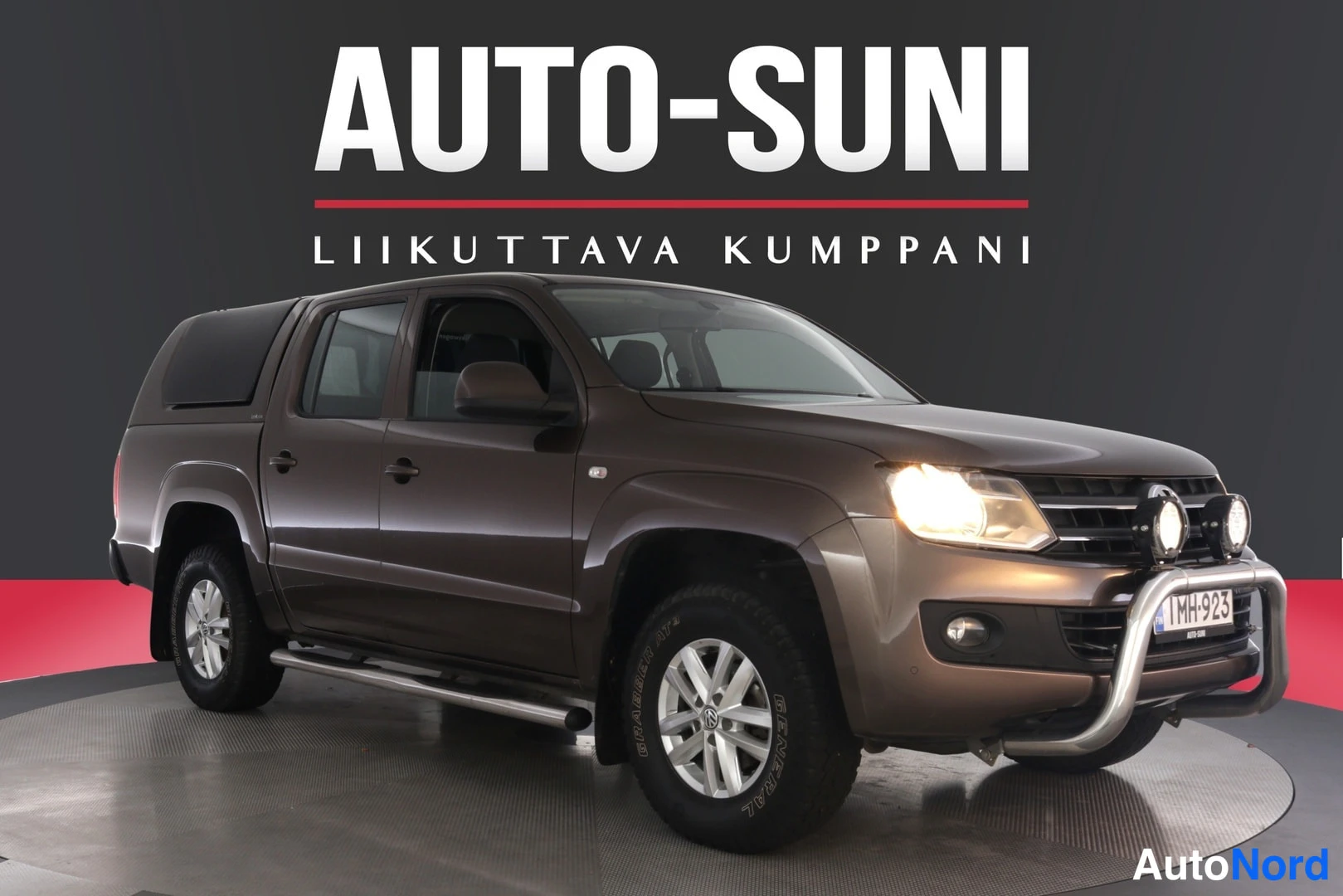 Etuviisto, nokka oikealle: Ruskea avolava-auto kuvattuna etuviistosta, keula oikealla; puskurissa tukkikaari ja sumuvalot, kyljessä astinlauta.