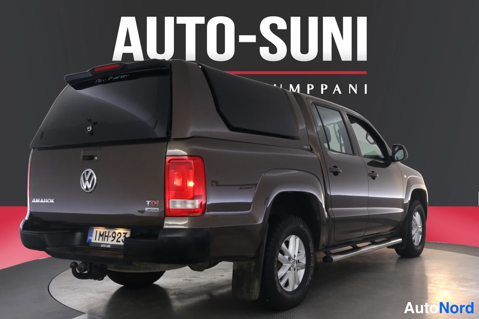 Takaviisto: Ruskenvärinen Volkswagen Amarok -lavallinen avolava-auto takaa sivulta kuvattuna, peruutusvalot päällä.