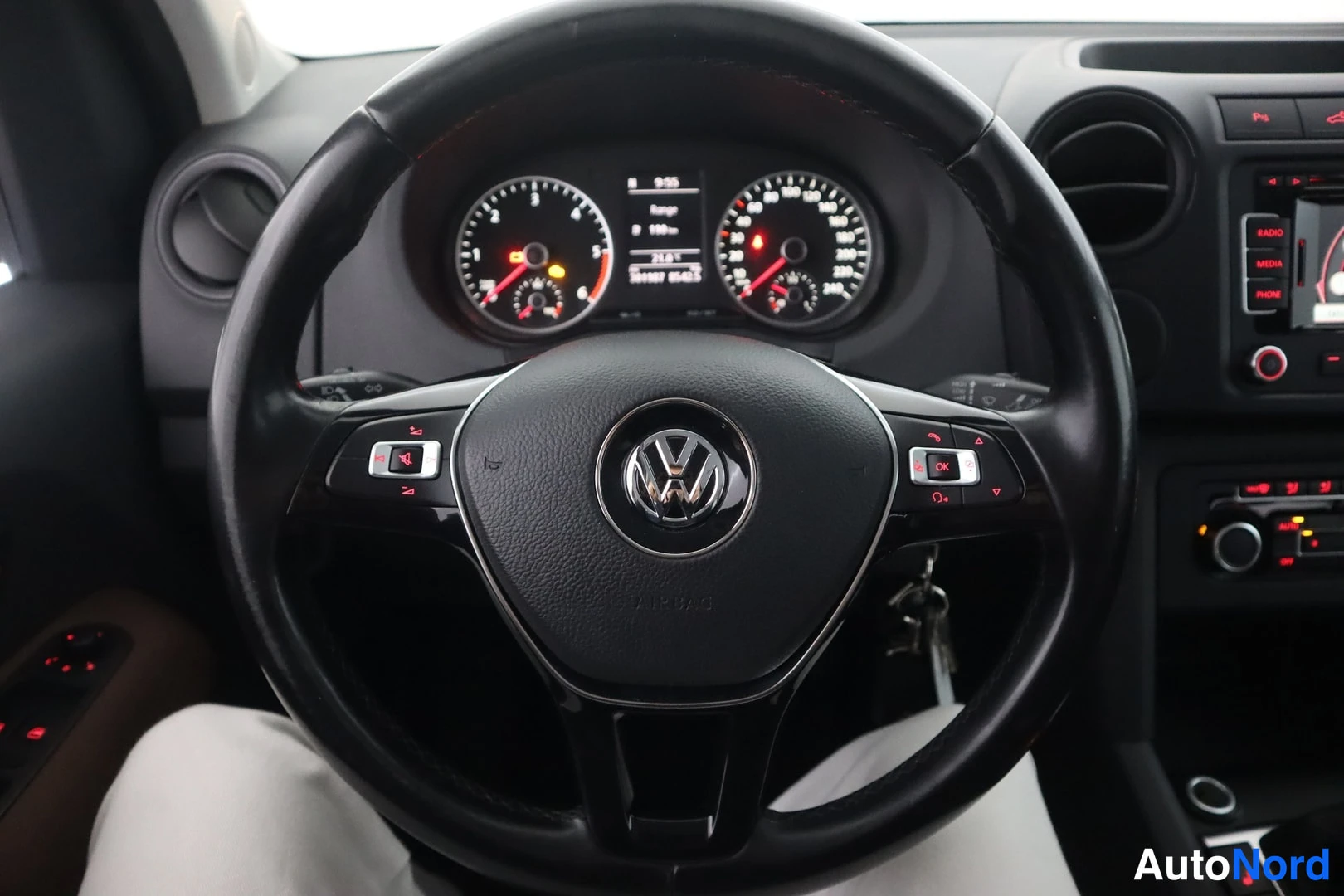 Etuviisto: Autojen sisätilat: Volkswagen-monitoimiohjauspyörä keskellä, takana kojelauta ja mittaristo, oikealla radionäyttö ja painikkeet RADIO, MEDIA ja PHONE.