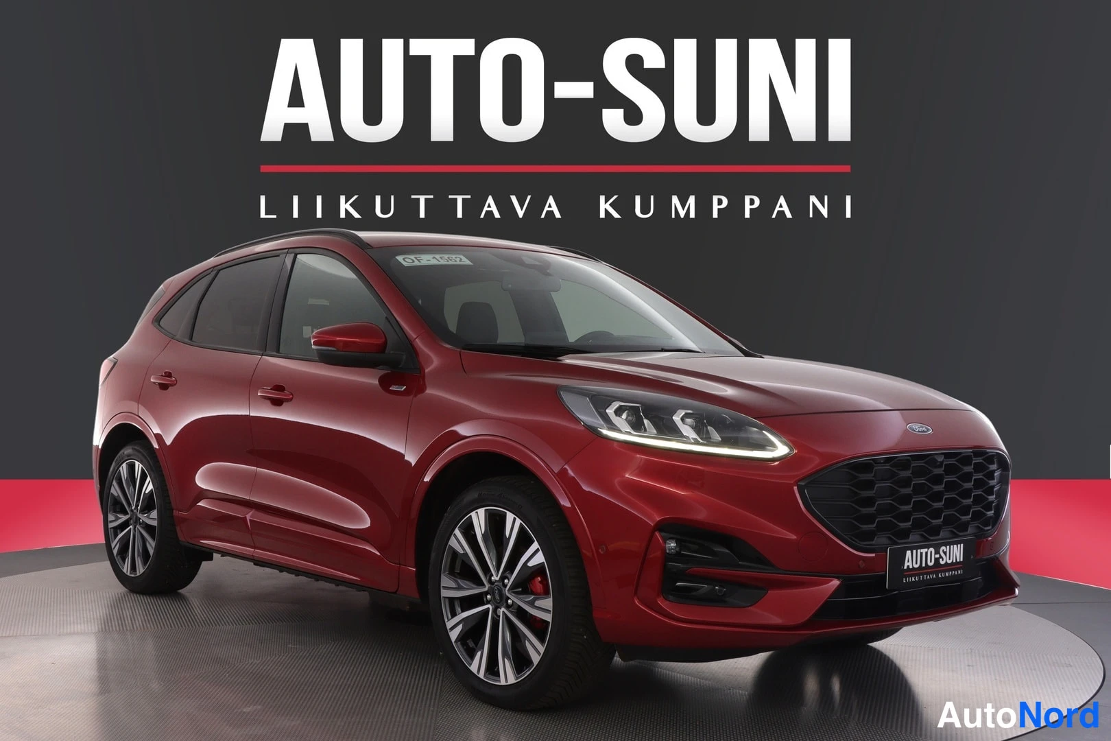 Etuviisto, nokka oikealle: Punainen Ford Kuga -henkilöauto kolmesta neljänneksestä etupästä oikealta kuvattuna studioissa, AUTO-SUNI-mainosteksti taustalla.