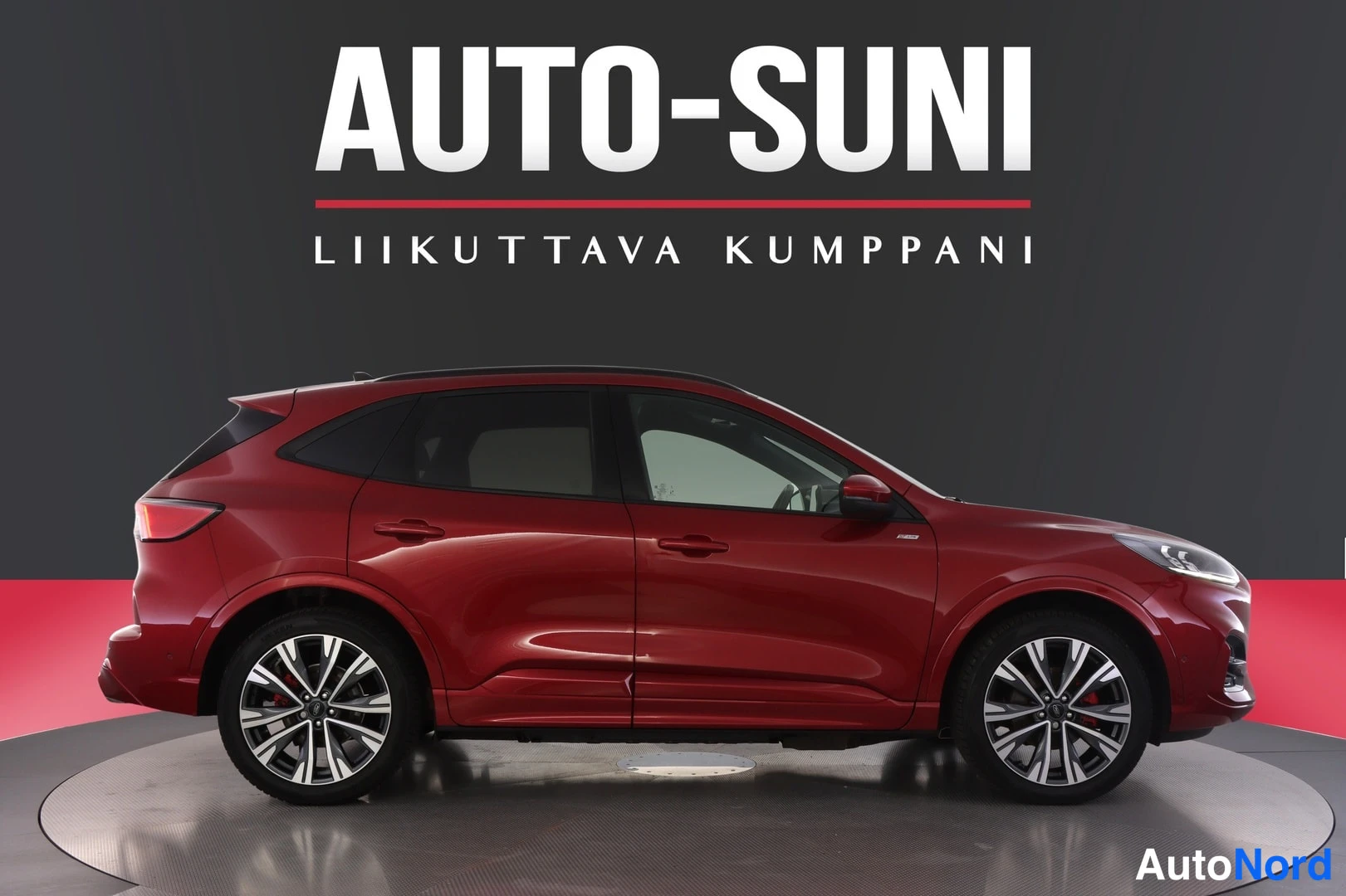 Sivulta: Punainen Ford Kuga -henkilöauto sivulta oikealta kuvattuna studioissa, AUTO-SUNI-mainosteksti taustalla.