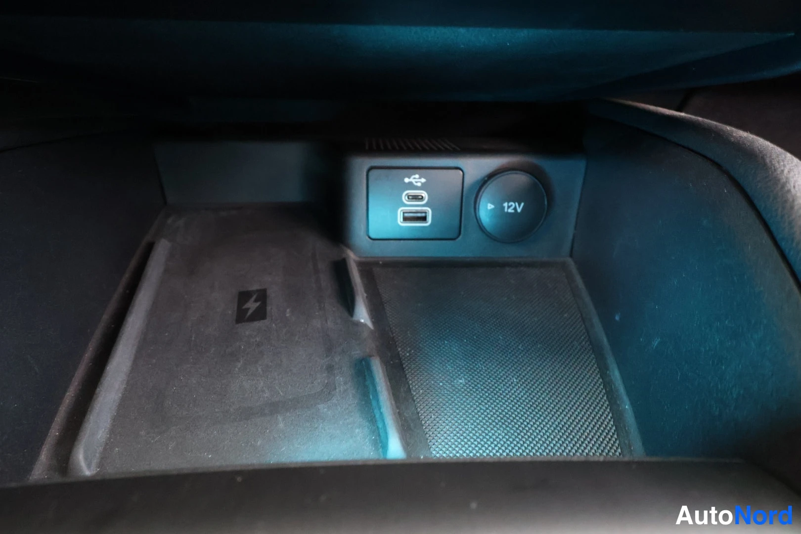 Yksityiskohta: Lokerikko, jossa USB-C-portti ja 12V-pistorasia sekä langattoman latauksen merkki (salama-kuvake).
