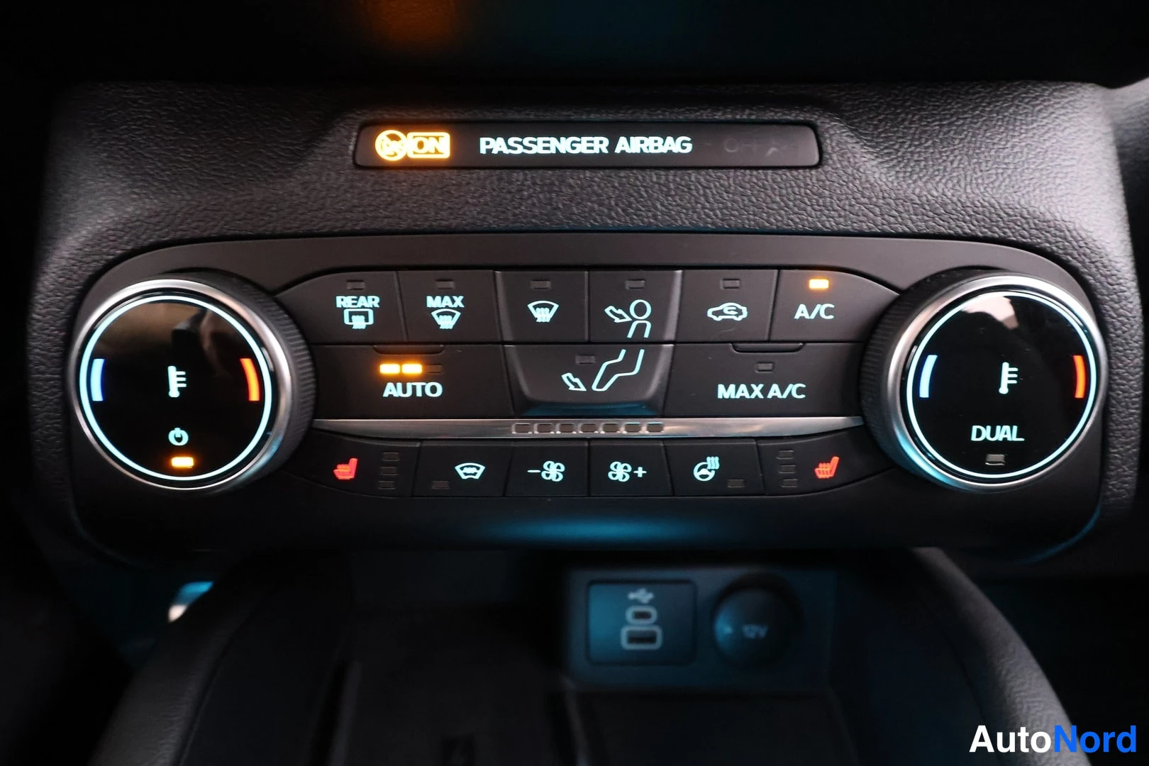 Yksityiskohta: Ilmastointilaitteen ohjauspaneeli, jossa kirjoitukset REAR, MAX, AUTO, MAX A/C, A/C ja DUAL, sekä ylhäällä PASSENGER AIRBAG -teksti ja ON-merkkivalo.