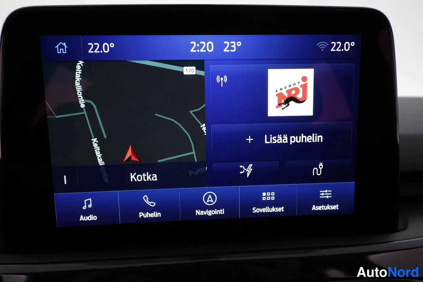 Muu: Ajoasemassa oleva keskiössä oleva kosketusnäyttö, jolla näkyy navigointikartta Kotkan alueelta, ENERGY NRJ -radiokanava sekä valikot Audio, Puhelin, Navigointi,