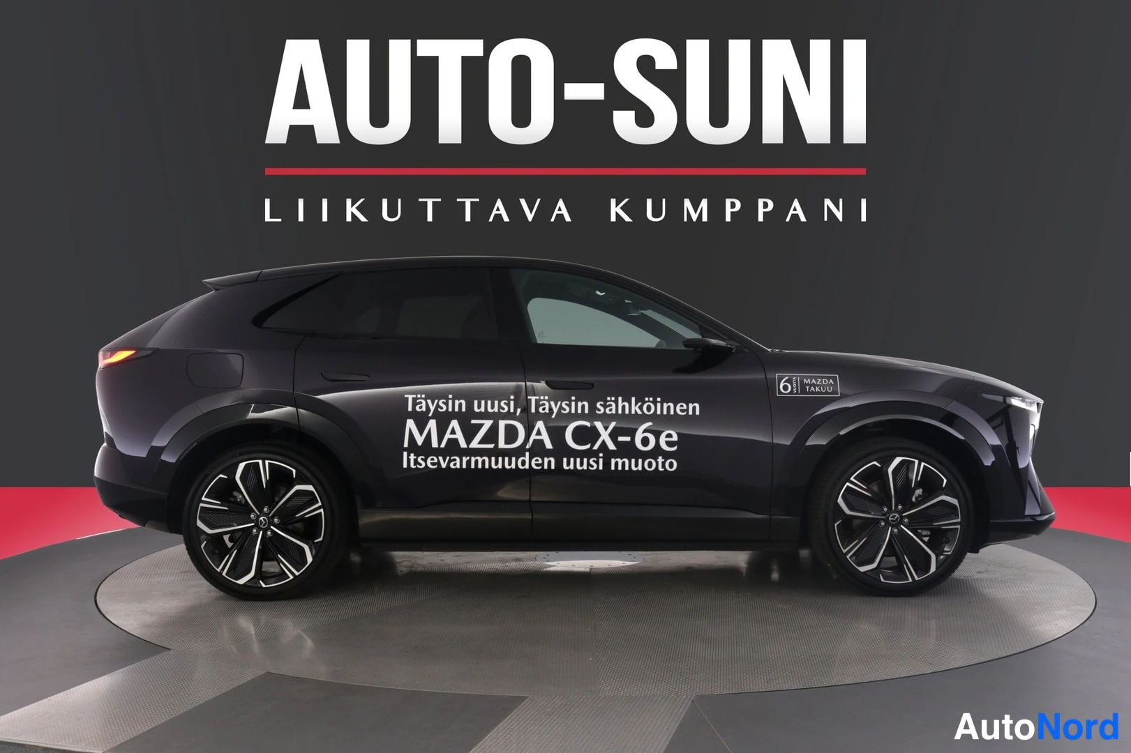 Sivulta: Musta Mazda CX-6e sivusta kuvattuna, kyljessä valkoinen mainosteksti ja Mazda 6 vuotta takuu -kyltti