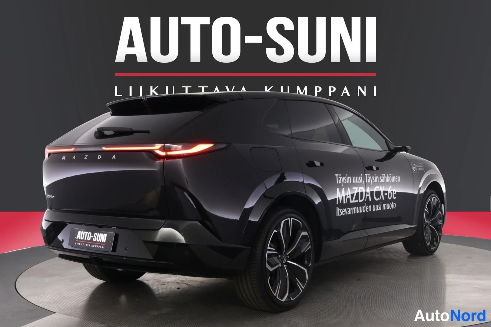 Takaviisto: Musta Mazda CX-6e takaviistosta oikealta kuvattuna, kyljessä mainosteksti ja keulassa Auto-Suni-kyltti