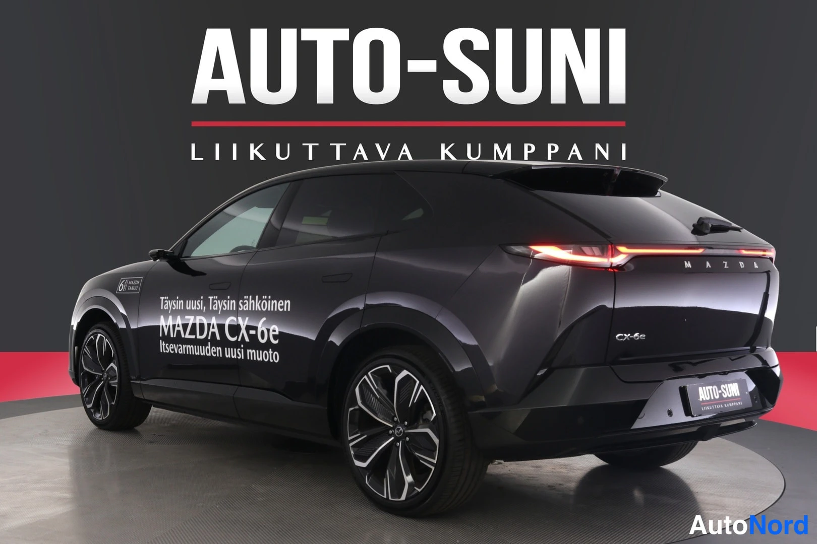 Takaviisto: Musta Mazda CX-6e takaviistosta vasemmalta kuvattuna, kyljessä mainosteksti ja keulassa Auto-Suni-kyltti