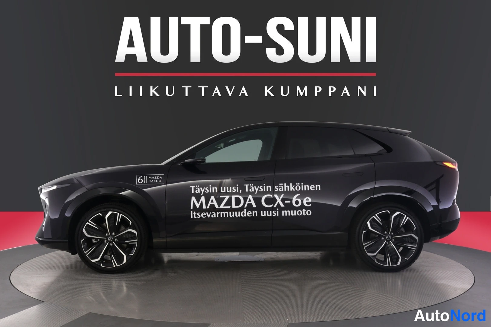 Sivulta: Mazda CX-6e etukautta vasemmalle, tumma kylki tummassa studioympäristössä.