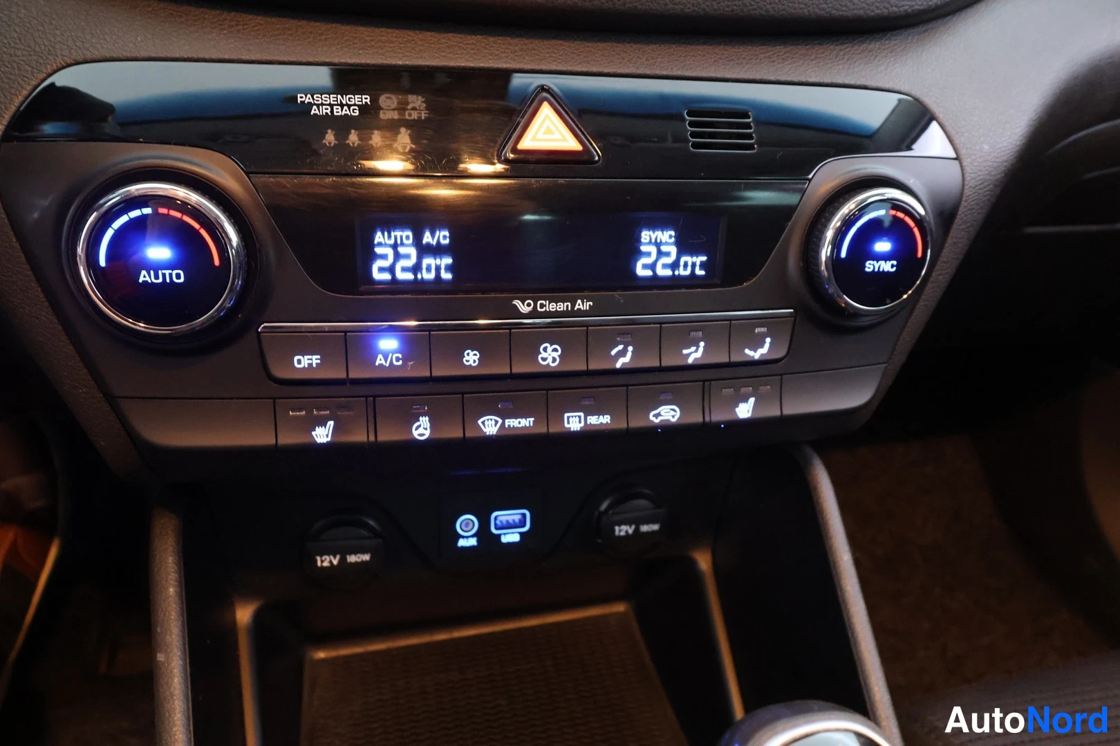 Muu: Auton keskiöodynamäkessä oleva ilmastointipaneeli, jossa näkyy syttyneet 22.0 °C lämpötilat, AUTO A/C-merkintä, nappien rivit (OFF, A/C, Clean Air), lämmitettäv
