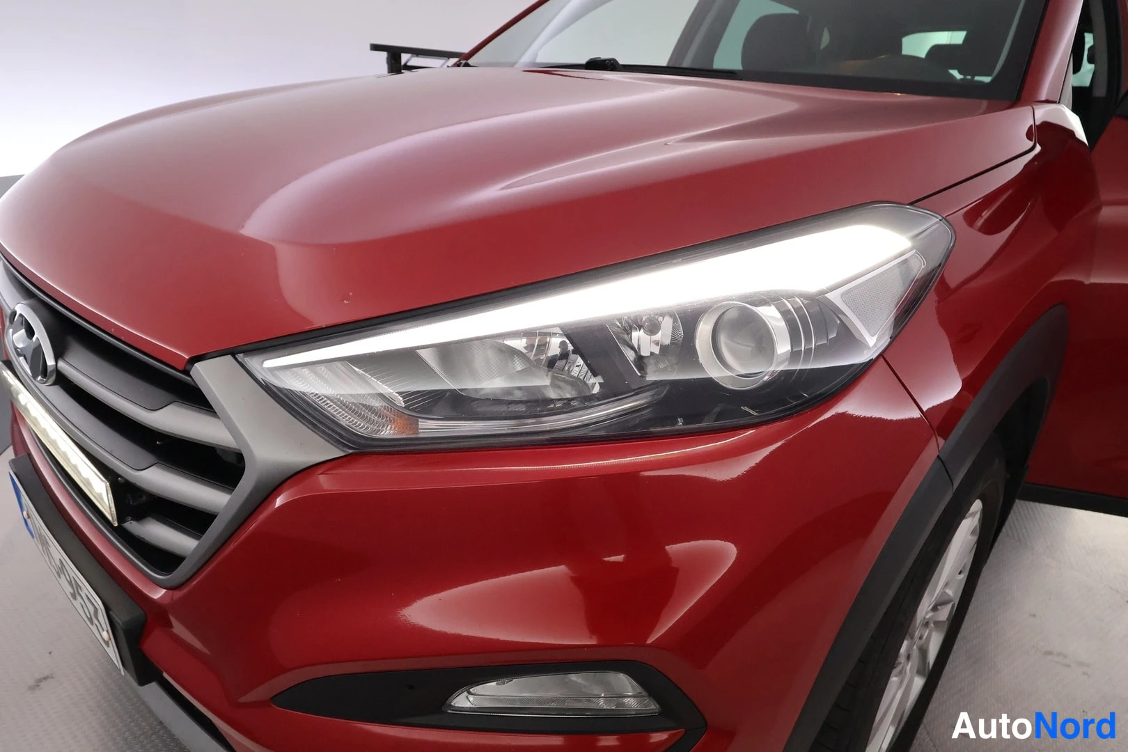 Edestä: Punanaisen auton keula lähikuvassa: etumoottoritila-ikkuna? Ei – kuva näyttää etusäleikön, Hyundai-logon ja päiväajovalon sisältävän ajovalon.