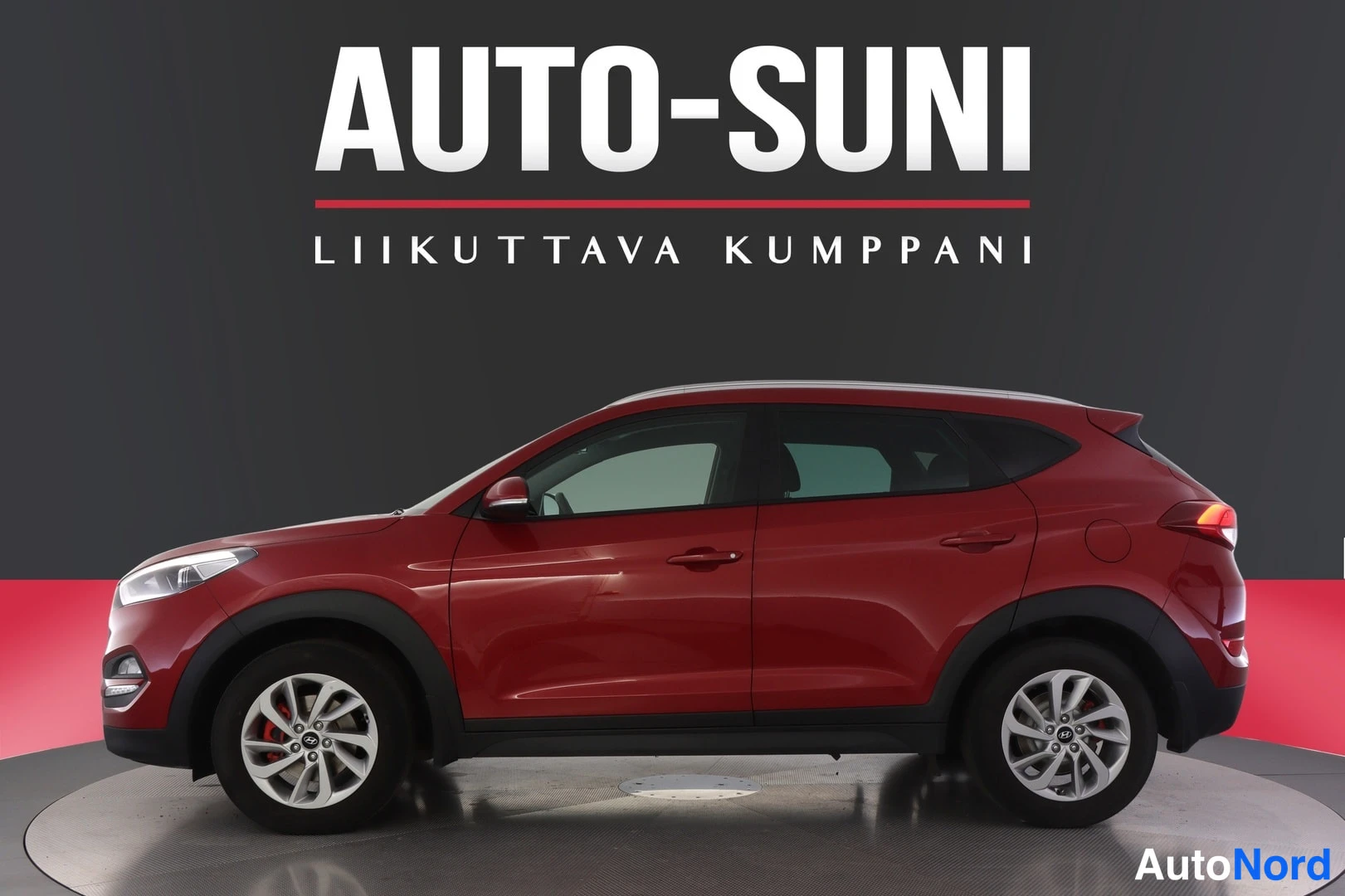 Etuviisto, nokka vasemmalle: Autosunin mainoskuva punaisesta Hyundai Tucson -maasturista kylkiasennossa tummaa taustaa vasten.