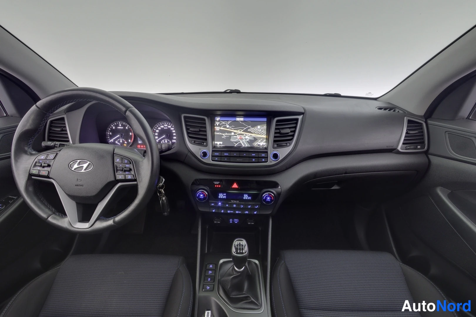 Muu: Hyundai Tucsan tumma kojelauta ohjaamosta kuvattuna: monitoimiOhjauspyörä, navigaatiokartta näytöllä, automaattinen ilmastointi ja manuaalivaihteen keila.