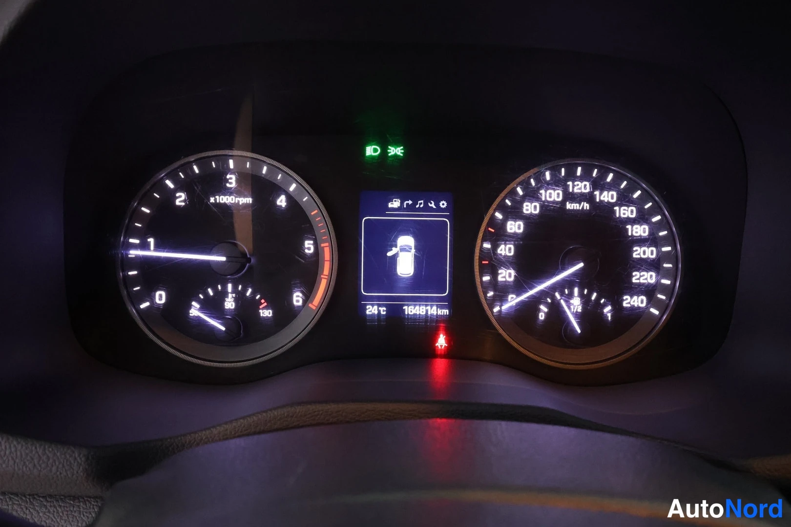 Yksityiskohta: Kojetaulu pimeässä: kierrosmittari x1000rpm 0-6, nopeusmittari 0-240 km/h, keskellä näyttö, jossa kirjaimellisesti 164814 km ja 24 °C.