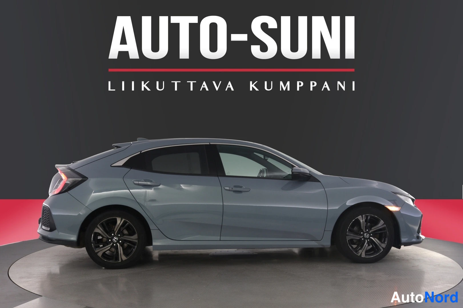 Etuviisto, nokka oikealle: Honda Civic -mallin viistoperäisen auton kylki- ja etunäkymä studiotaussa; auto on harmaansininen ja siinä on tummat kevytmetallivanteet.