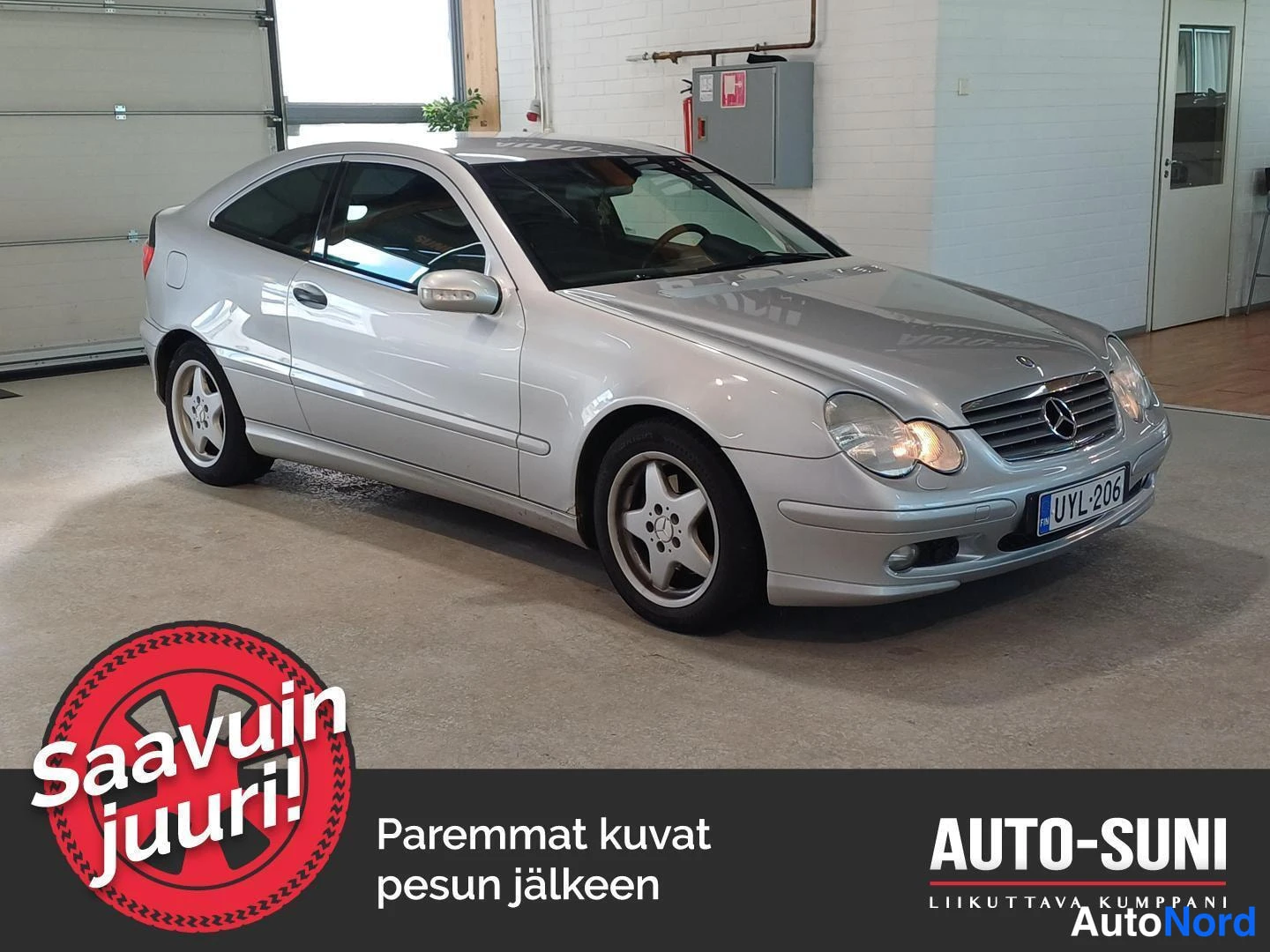 Etuviisto, nokka oikealle: Silver Mercedes-Benz CLC/C-Class coupe photographed from the front-three-quarter angle in a showroom, showing the front grille, headlights, left flank