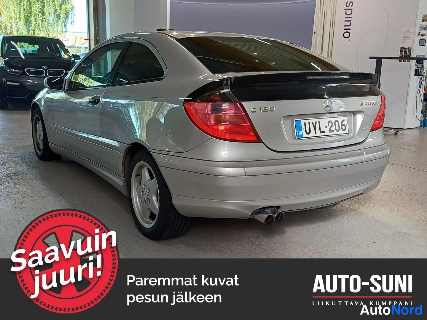 Takaviisto: Rear three-quarter view of a silver two-door coupe from the left rear showing tail lights, trunk lid with C180 and Kompressor badges, rear bumper, dual exhaust
