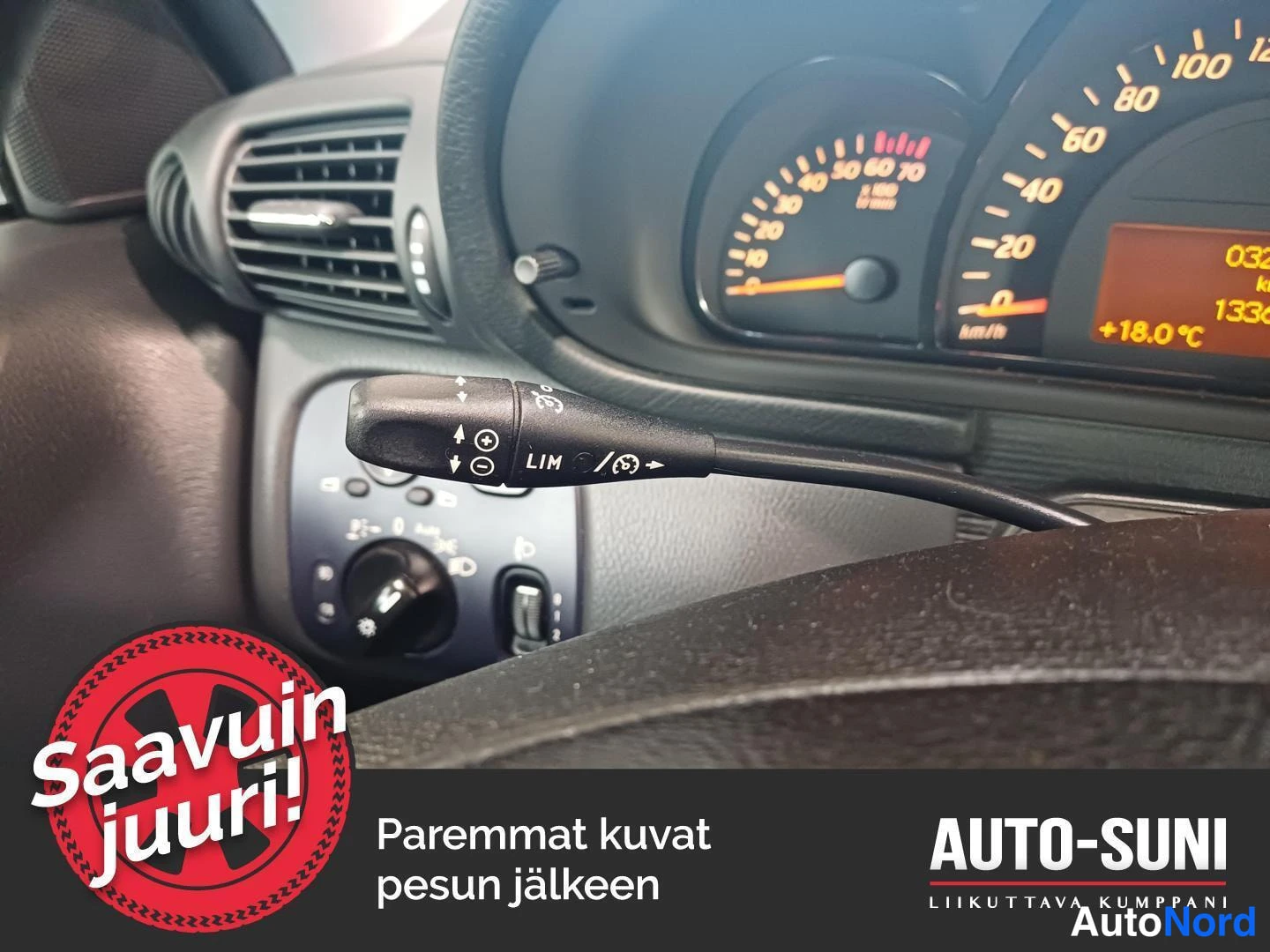 Yksityiskohta: Steering stalk on the left side of the steering column with CRUISE CONTROL buttons (LIM, +, -) and symbols for headlight/indicator functions. Dashboard and air