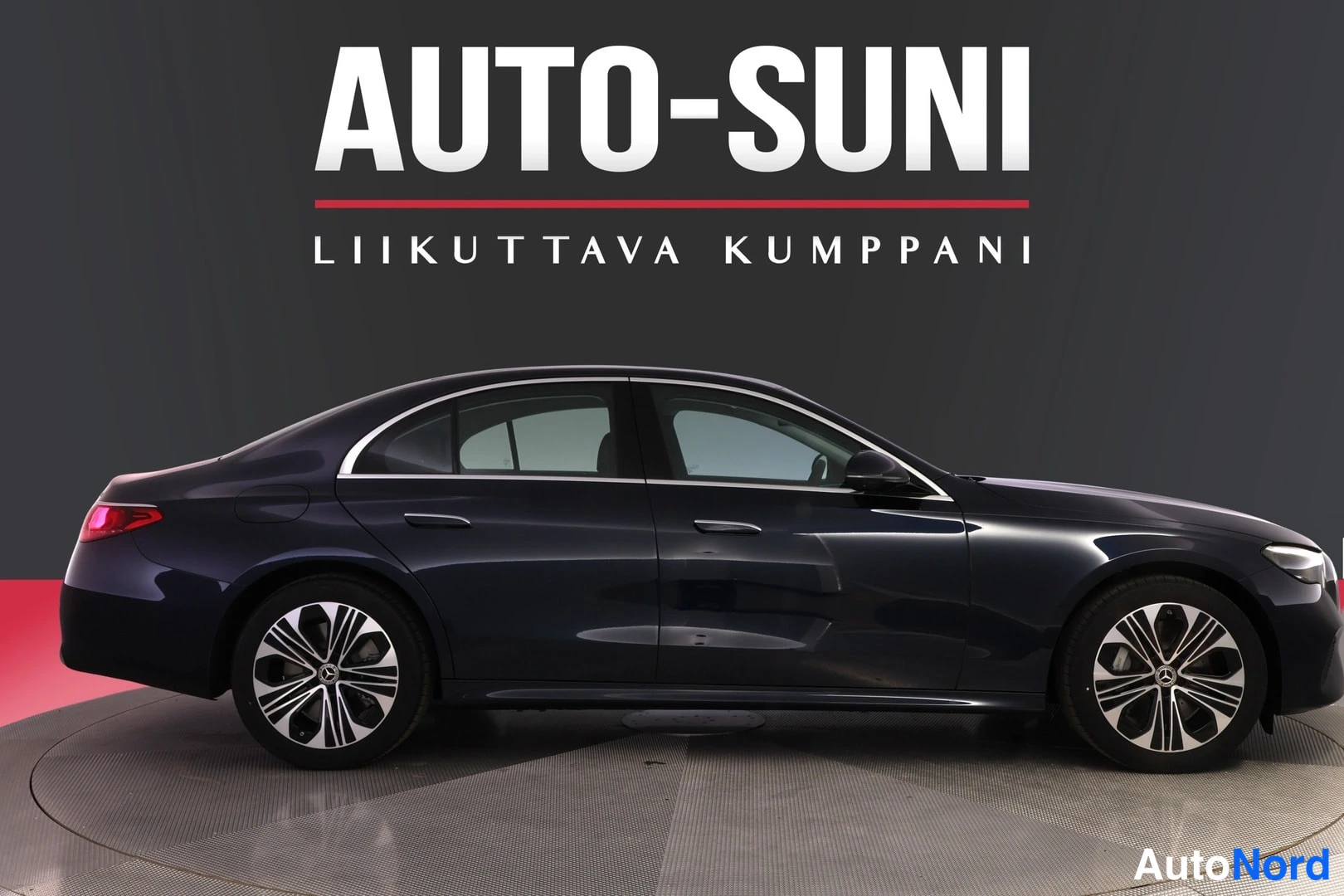 Sivulta: Tummansinisen sedanin sivuprofiili studiotakustalla, AUTO-SUNI-mainoslogo taustalla.