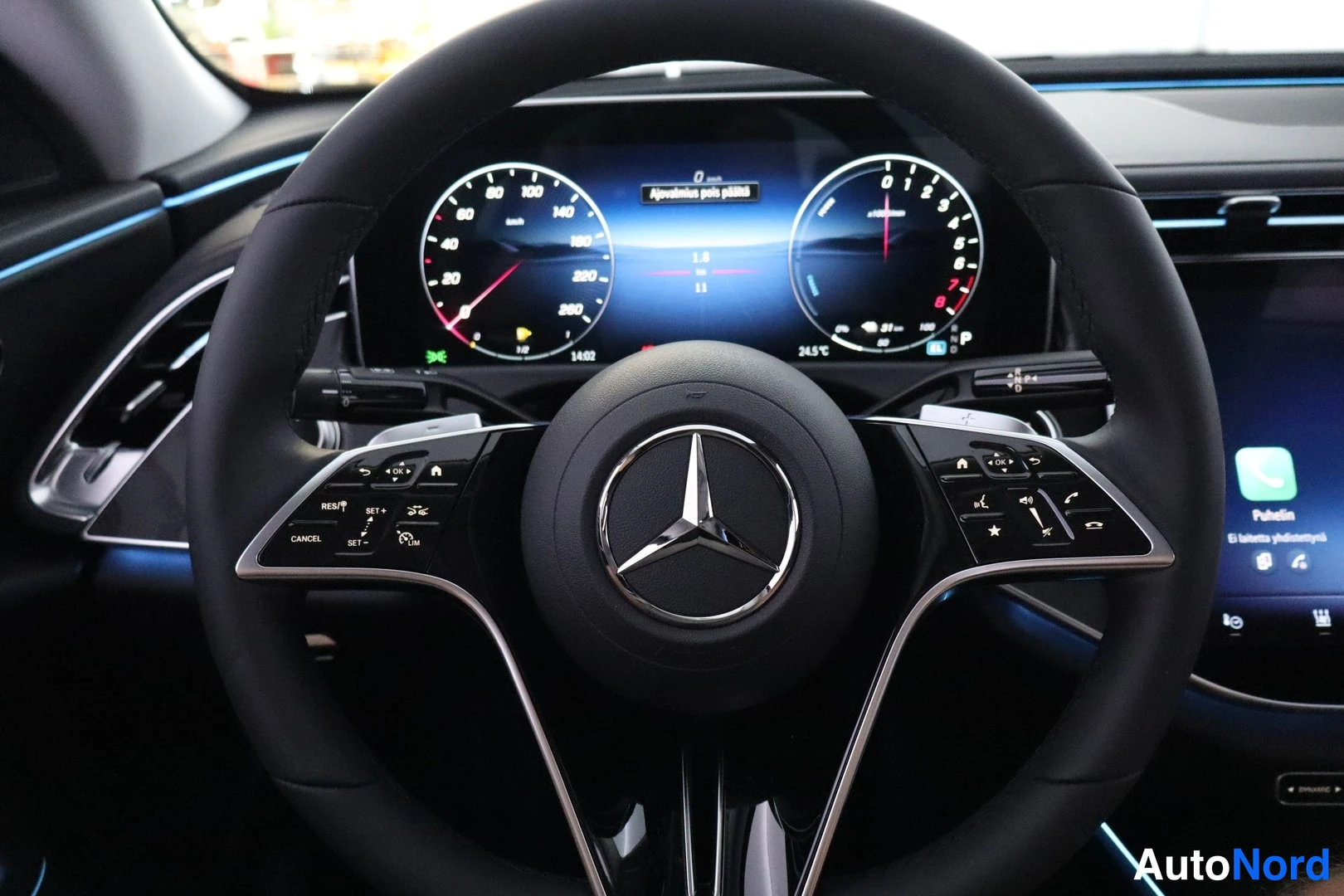 Sivulta: Mercedes-Benz leather steering wheel with digital cockpit behind, MBUX screen showing phone 'Puhelin' menu, dark cabin