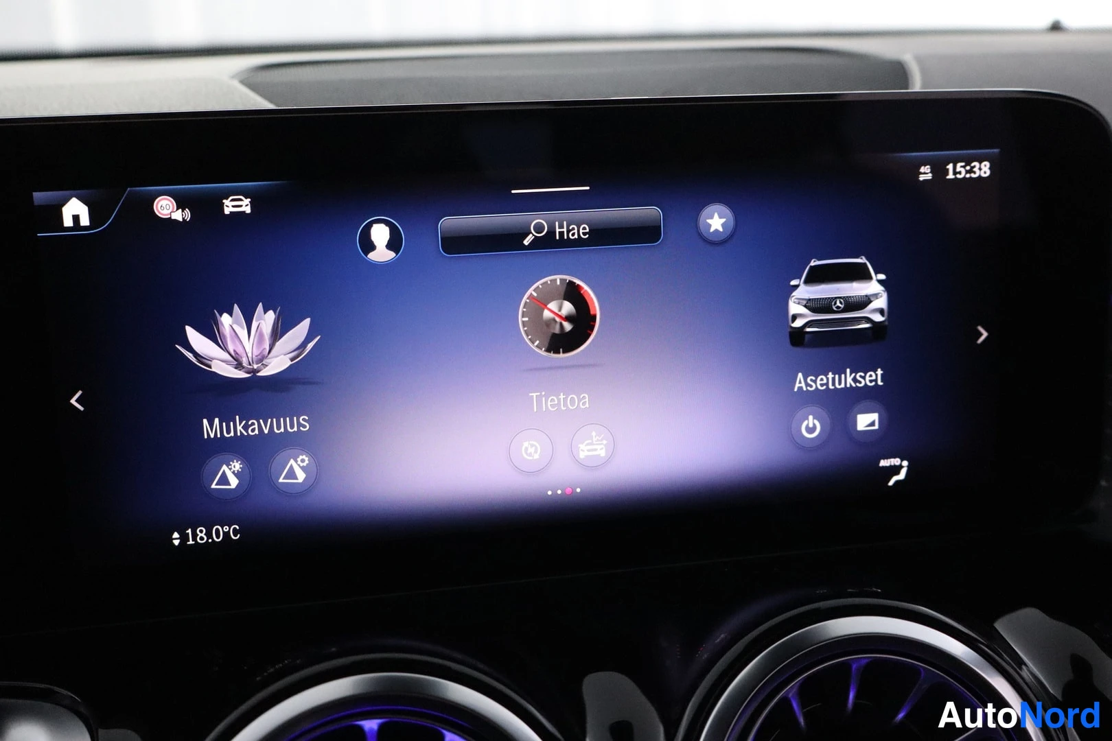 Muu: Mercedes-Benzin keskikonsolin infotainment-näyttö, jossa näkyvät valikot Mukavuus, Tietoa ja Asetukset sekä hake-kenttä; näytön alapuolella kaksi pyöreää ilmast