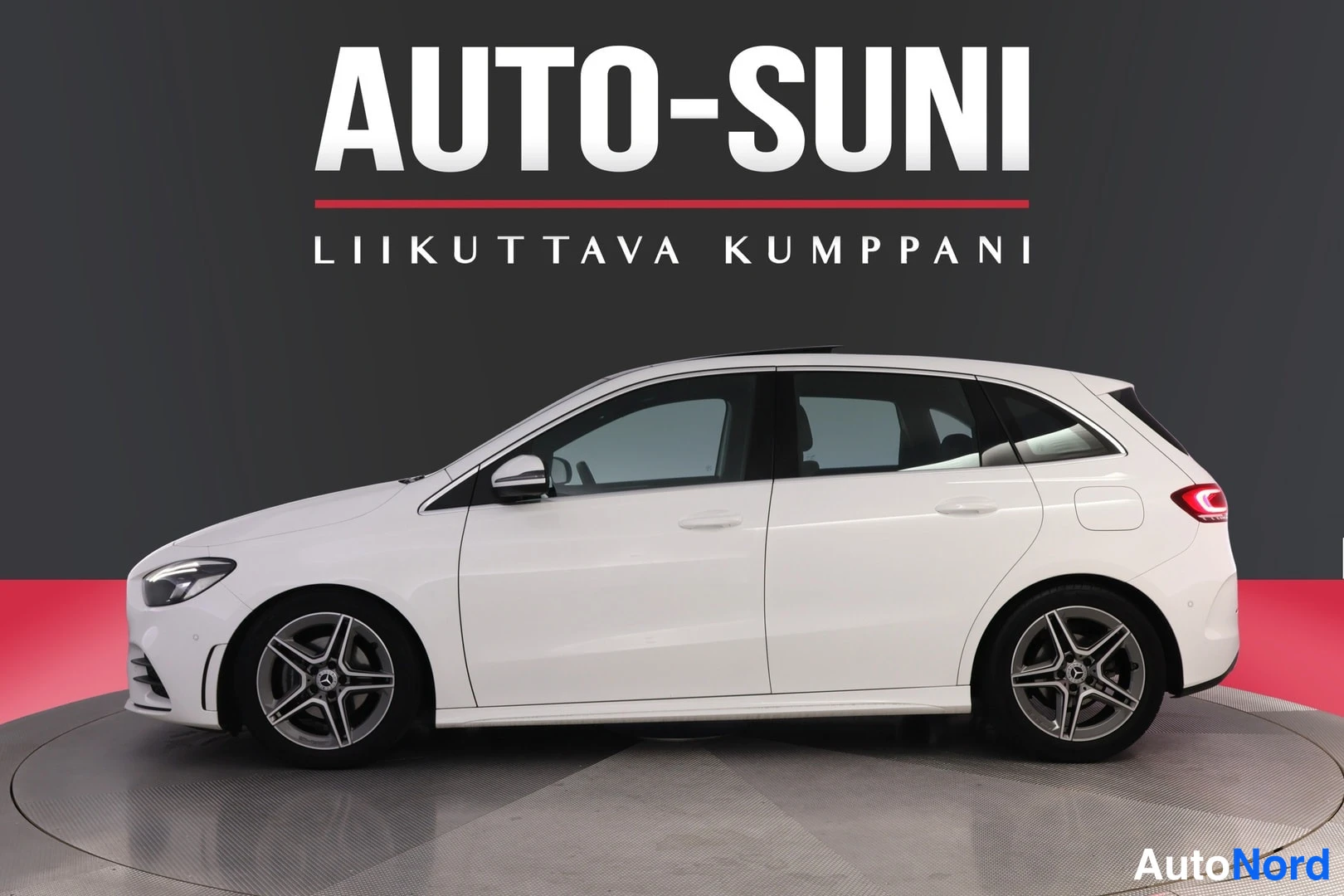 Sivulta: Valkoisen tila-auton sivukuva studio­taustaa vasten, AUTO-SUNI-logo yläosassa. Autossa on panoraamalasikatto ja moni­osaiset kevytmetallivanteet.