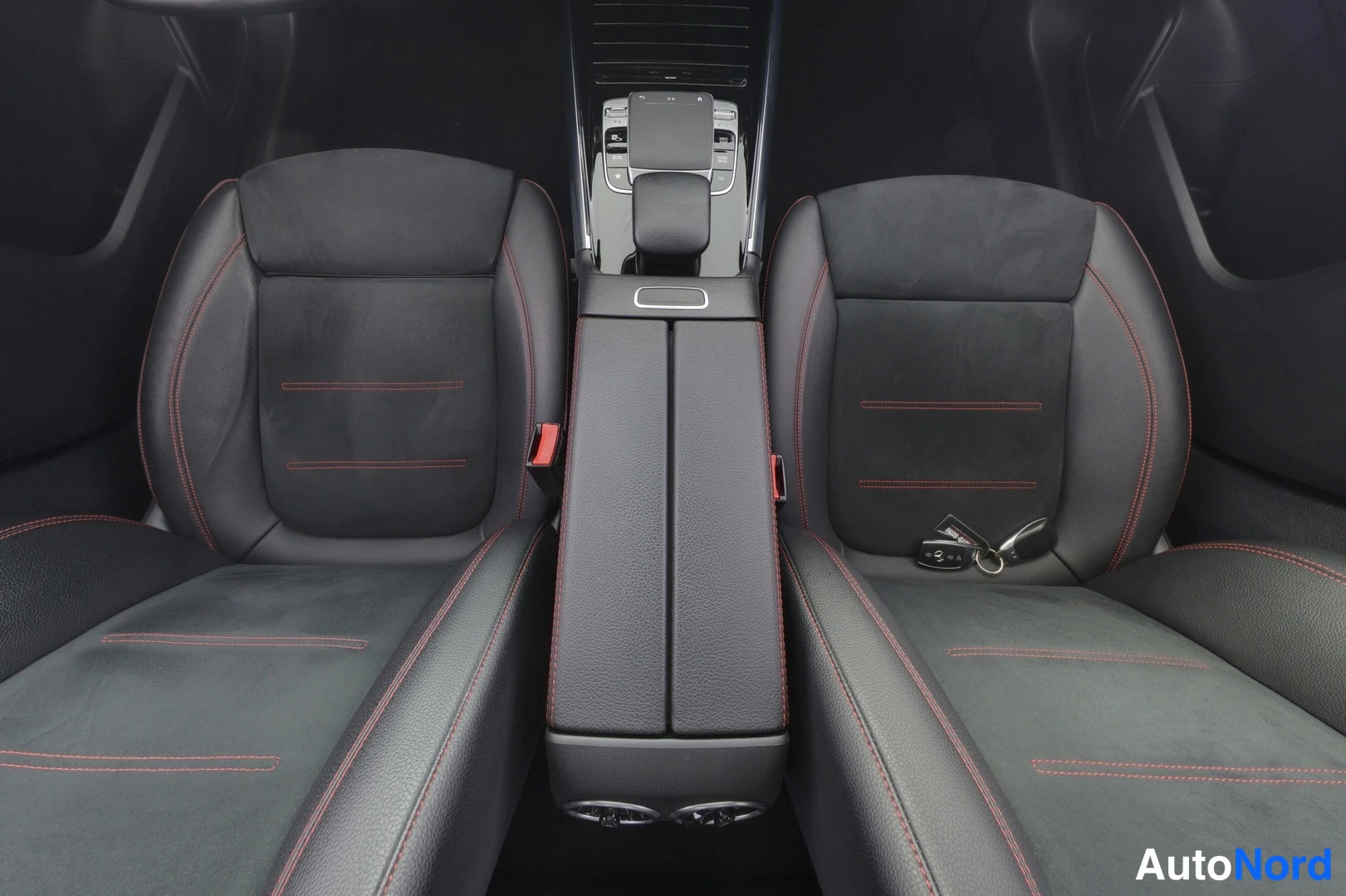 Etuistuimet: Front view of two front seats in black leather with red contrast stitching and an armrest between them.