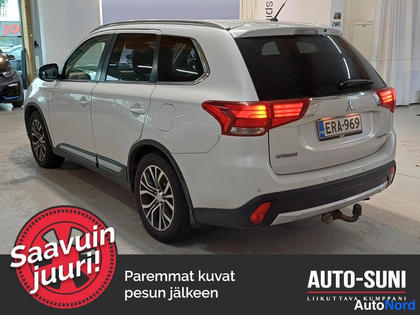 Takaviisto: Valkoinen Mitsubishi Outlander -maastauto sisätiloissa, takaosa vasemmalla näkyvissä.