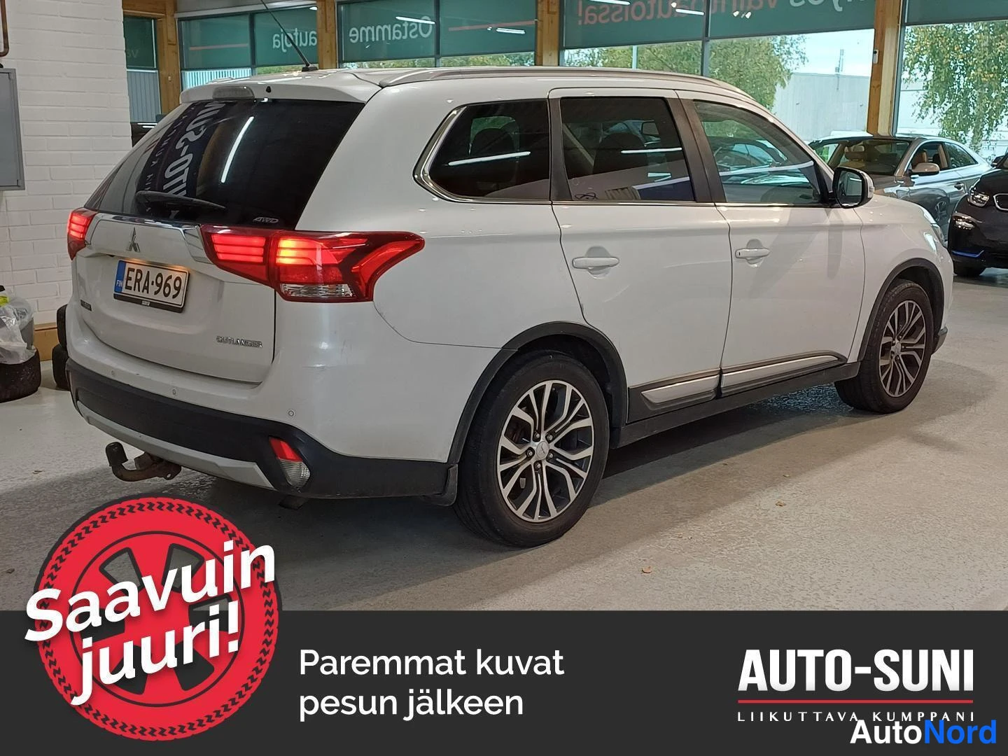 Takaviisto: Valkoinen Mitsubishi Outlander -maastauto sisätiloissa, takaosa oikealla näkyvissä.