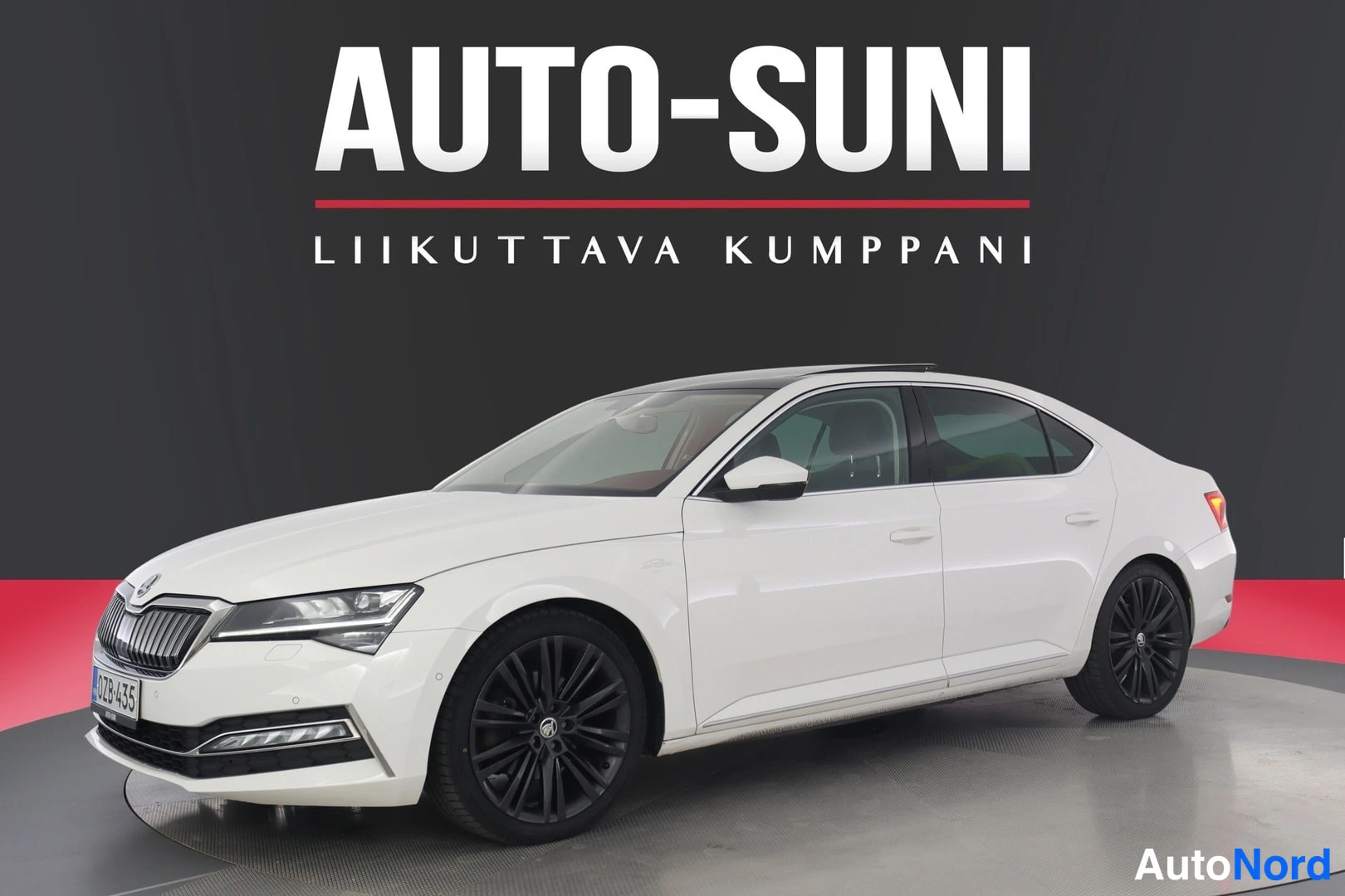 Etuviisto: Valkoinen sedan kolmasosakulmasta edestä vasemmalta, mustat vanteet ja lasikatto, harmaa kuvatausta kirjaintekstillä AUTO-SUNI.