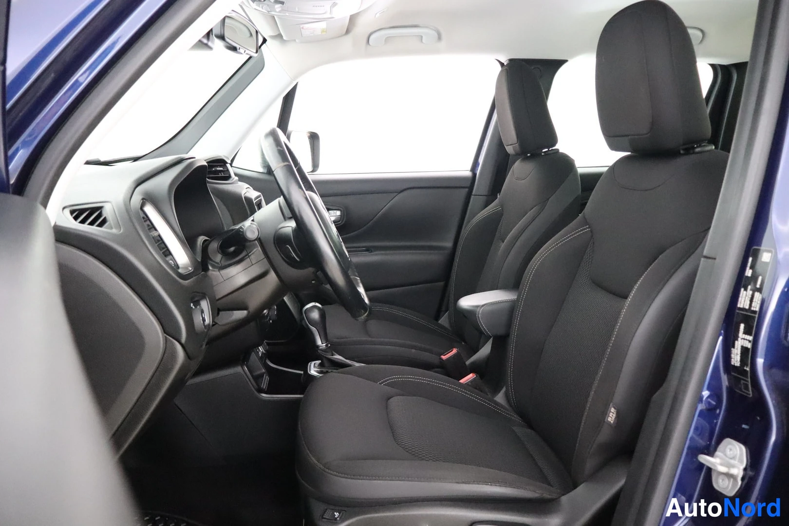 Muu: Kuljettajan puolen sisätila: musta ohjauspyörä, kojelauta ja mustat kangasistuimet, ovipellin avattuna.