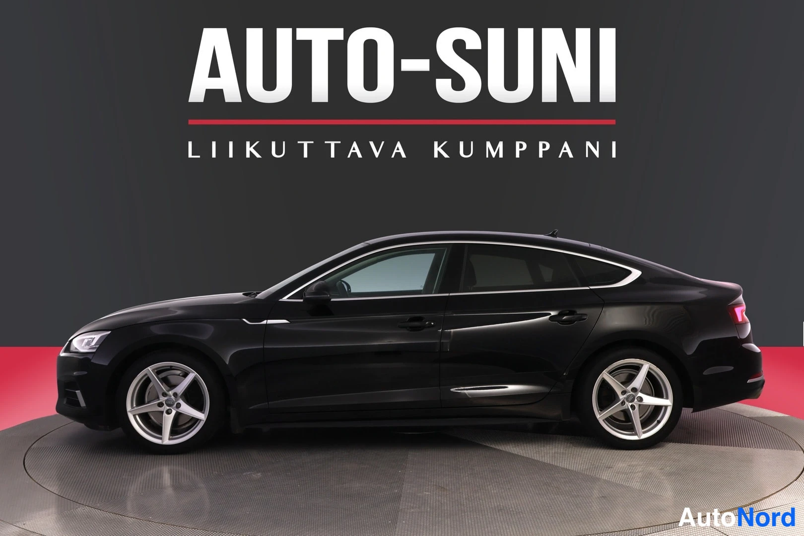 Takaviisto: Mustan Audi A5 Sportbackin sivukuva studiotaustaa vasten, auton koko sivuprofiili näkyvissä.