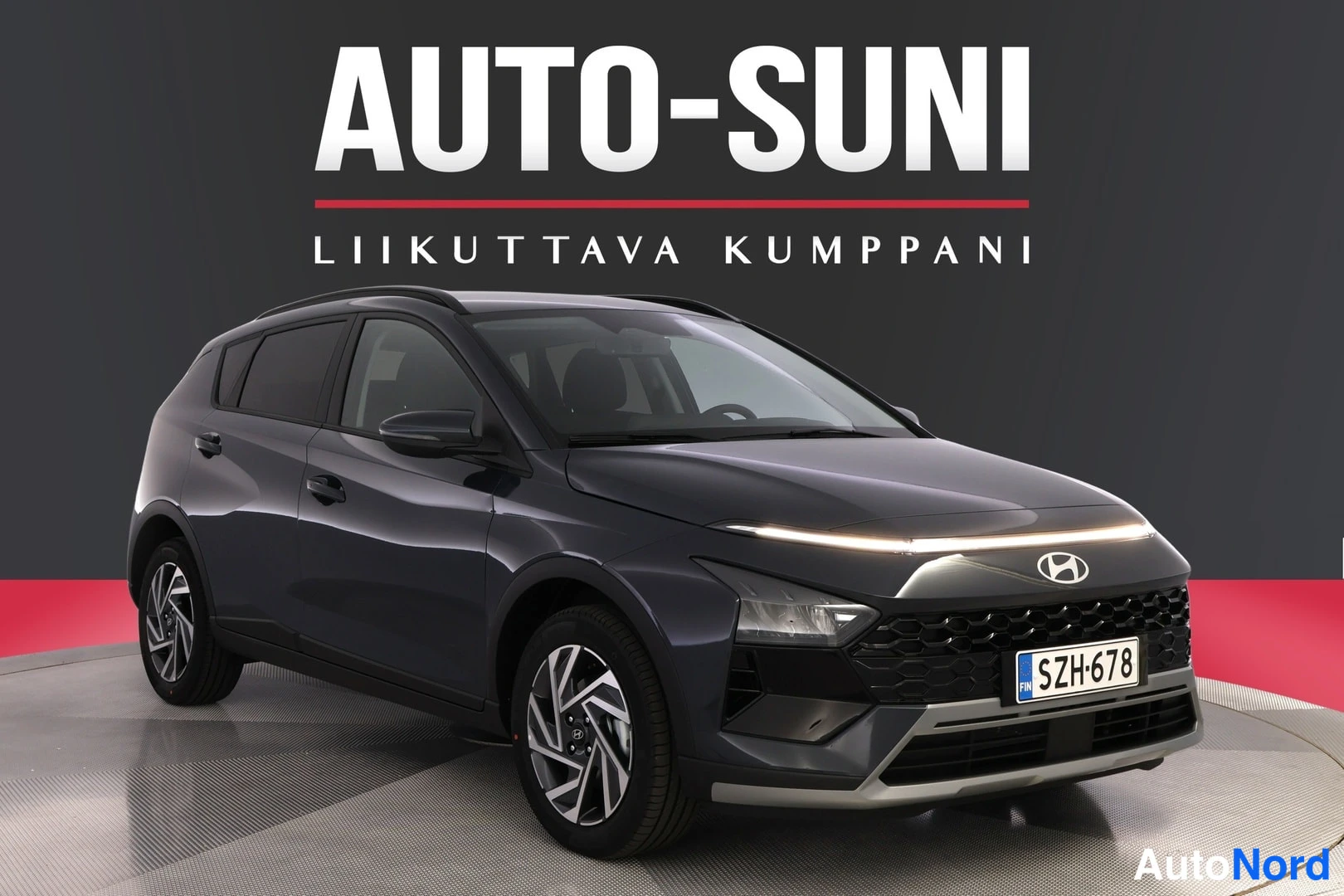 Etuviisto, nokka oikealle: Auton etukulmanosto: tummanharmaa hyttinen rekisterillä, etusäleikkö ja ajovalot näkyvissä oikealla, studiovaalea pohja ja AUTO-SUNI-tunnus taustalla.