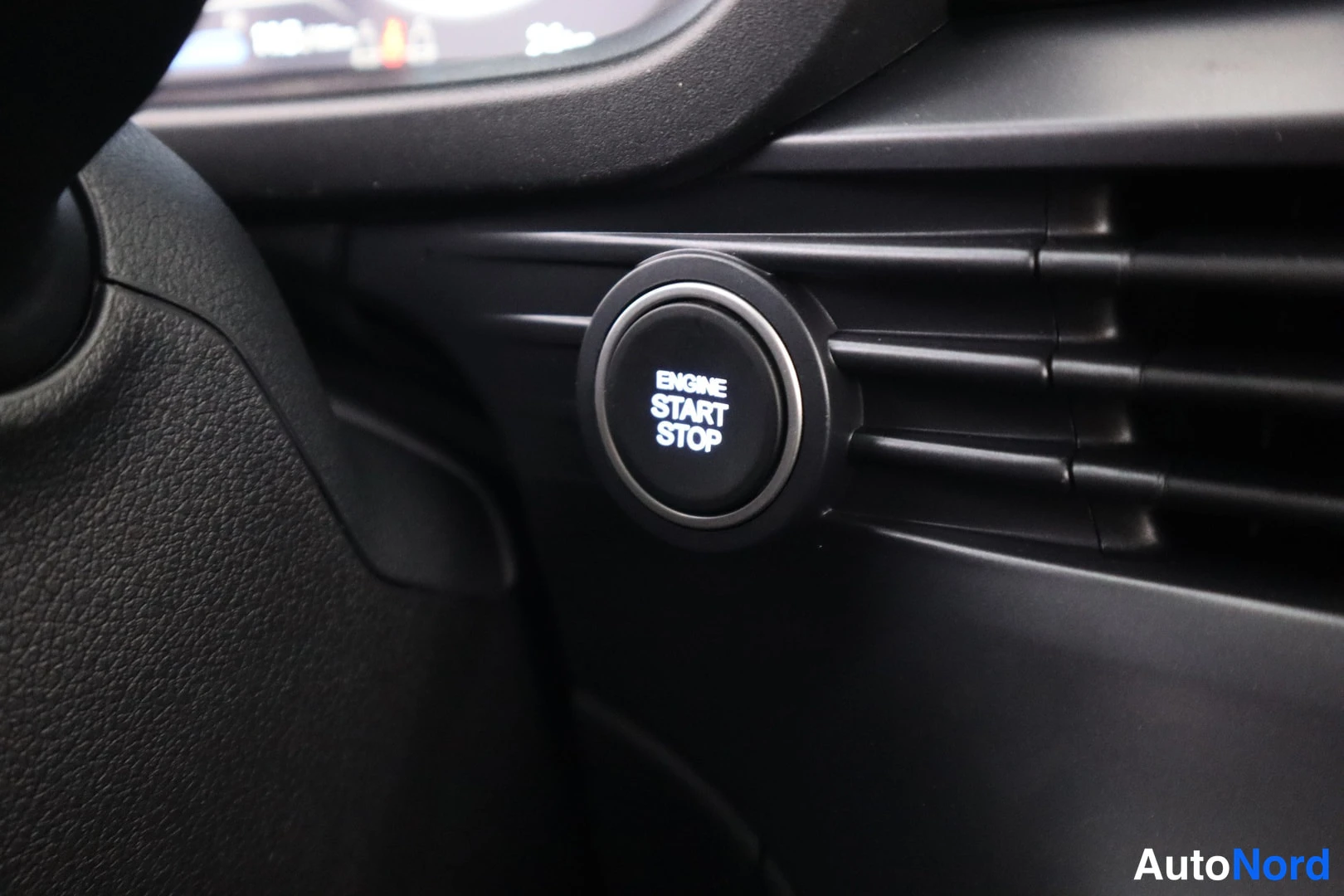 Muu: Lähikuva avaimettoman käynnistyksen painikkeesta, jossa teksti ENGINE START STOP, ohjauspyörän ja tuuletusritilän vieressä.