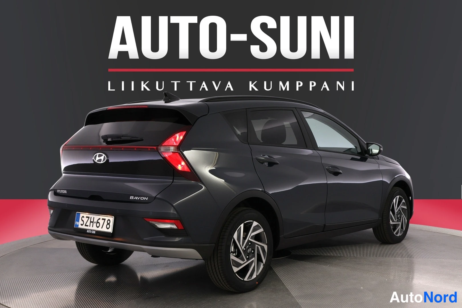 Takaviisto: Auton takakulmanosto: tummanharmaan BAYONin takavalot, Hyundai-merkki ja rekisterikilpi näkyvissä vasemmalla, oikealla kylki.