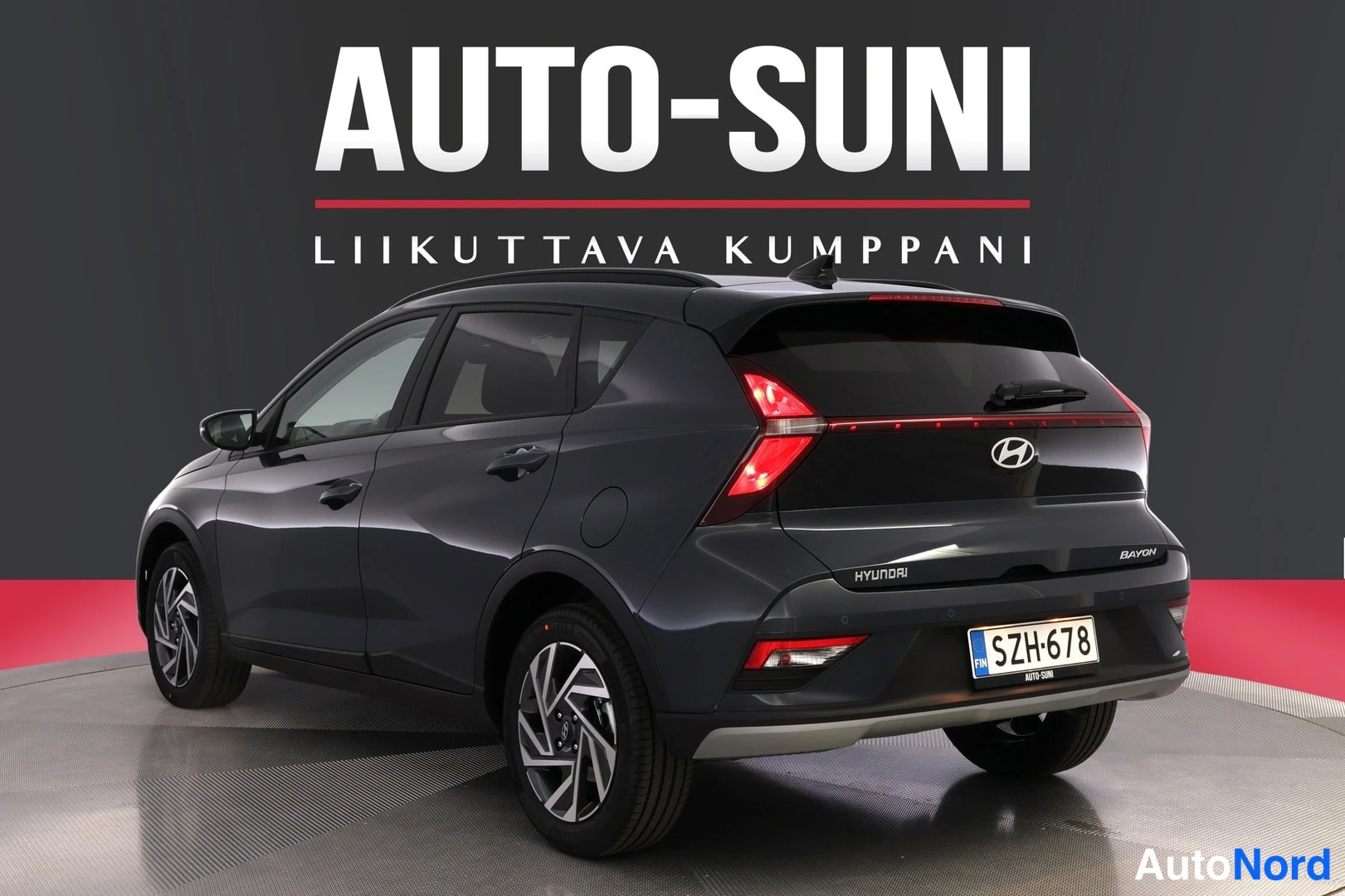 Takaviisto: Auton takakulmanosto oikealta: tummanharmaan BAYONin takavalo, Hyundai-merkki ja rekisterikilpi oikealla, vasen kylki ja pyörät näkyvissä.