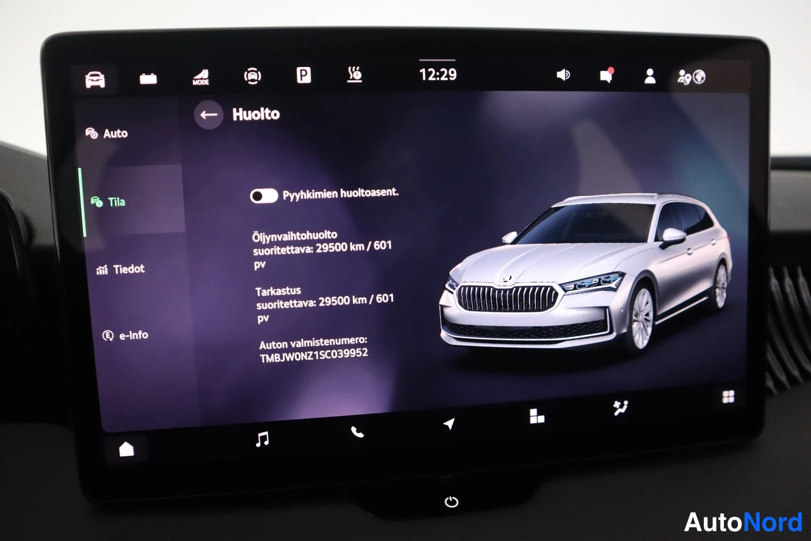 Yksityiskohta: Car infotainment screen in maintenance mode ('Huolto'). Text displays upcoming oil service at 29500 km, inspection due at 601 days, and the vehicle identificati