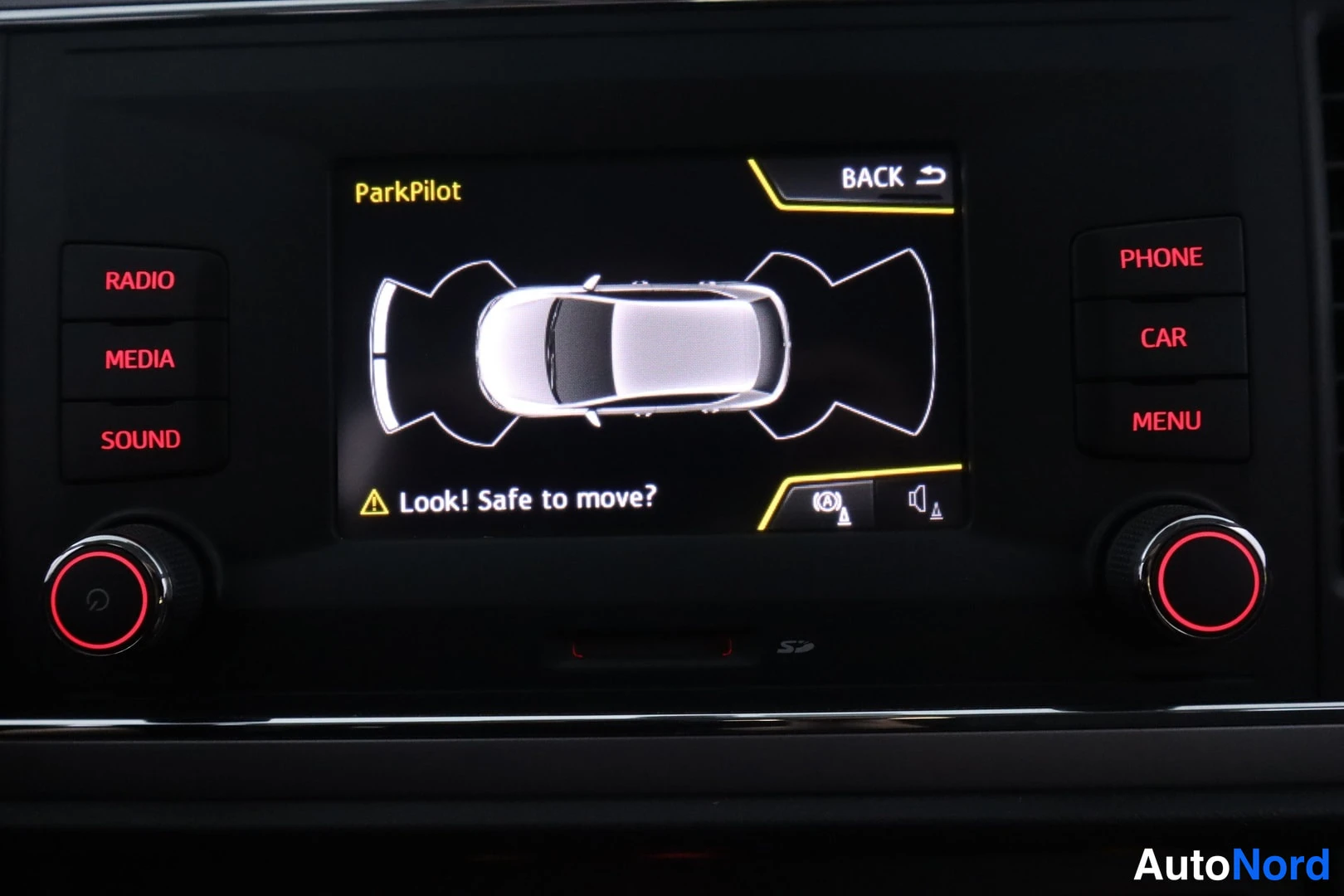 Muu: Infotainment-näyttö ParkPilot-törmäysvaroituskuvalla: 'Look! Safe to move?' -teksti, RADIO/MEDIA/SOUND- ja PHONE/CAR/MENU-napit.
