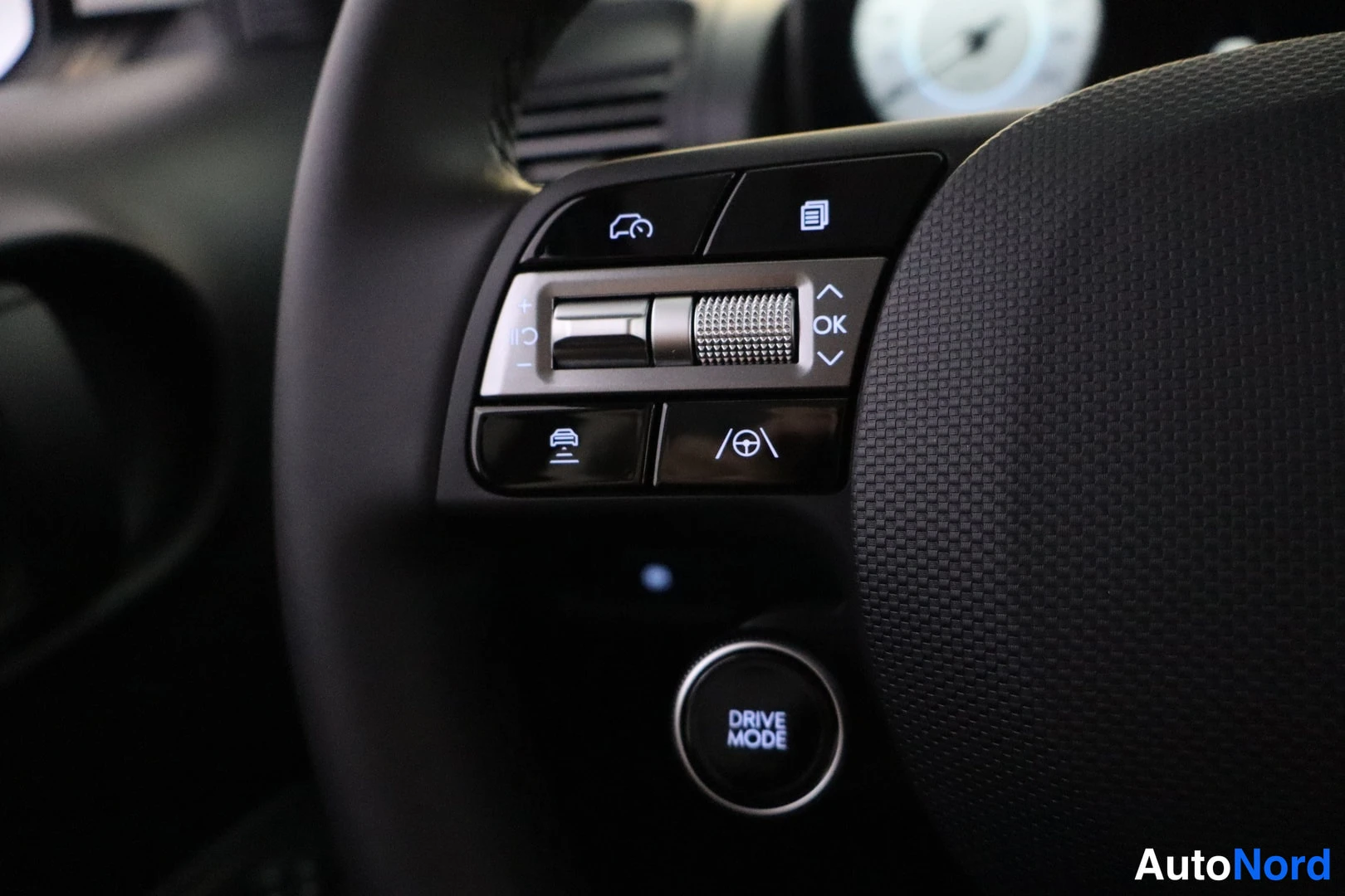 Muu: Ohjauspyörän vasemman puhallinpaneelin painikkeet lähikuvassa, mm. OK-näppäin, ajoneuvo- ja matkailunäytön symbolit sekä DRIVE MODE -painike.