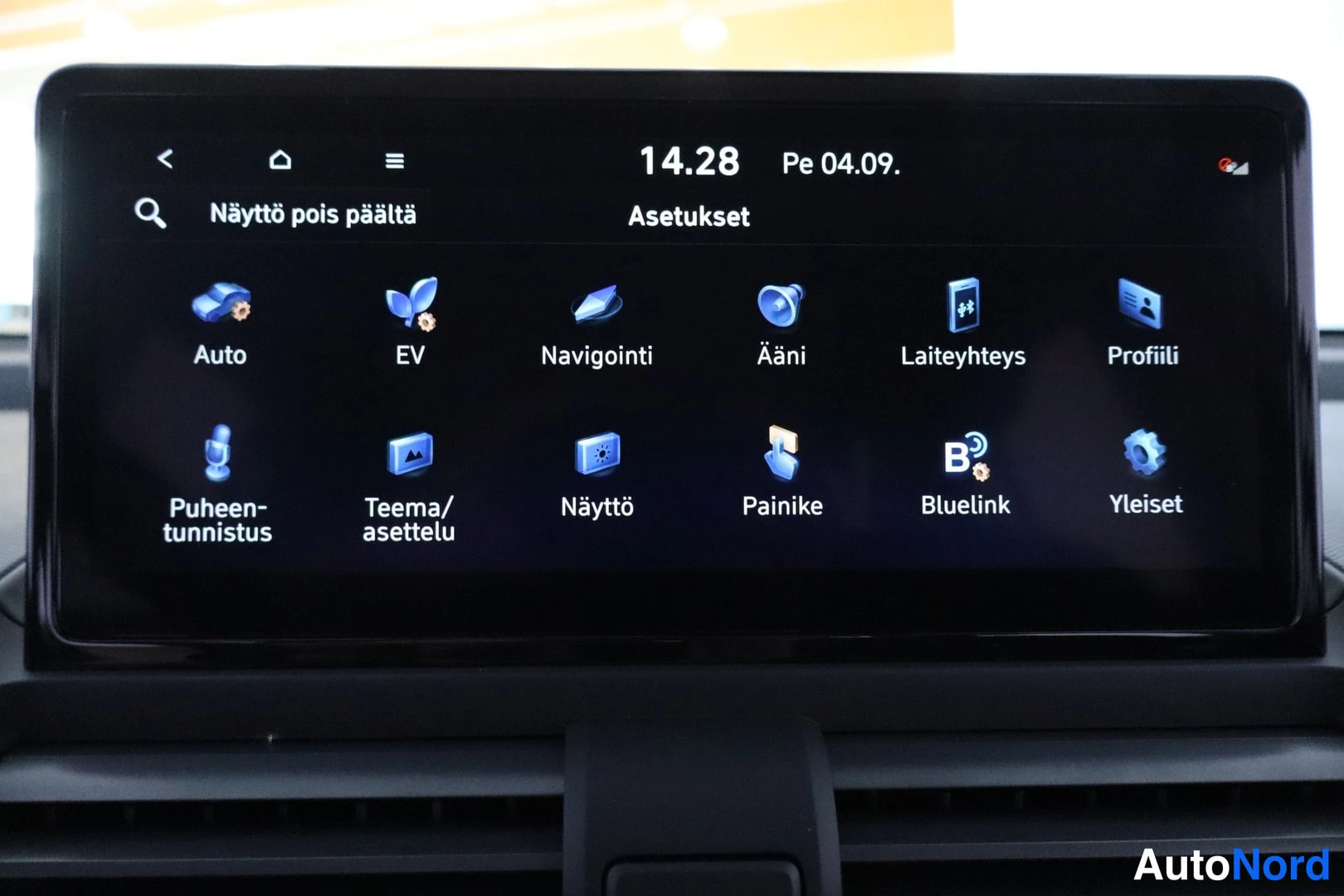 Muu: Mustavalkoinen kosketusnäytön Asetukset-valikko kuvakkeineen kuten Auto, EV, Navigointi ja Bluelink.