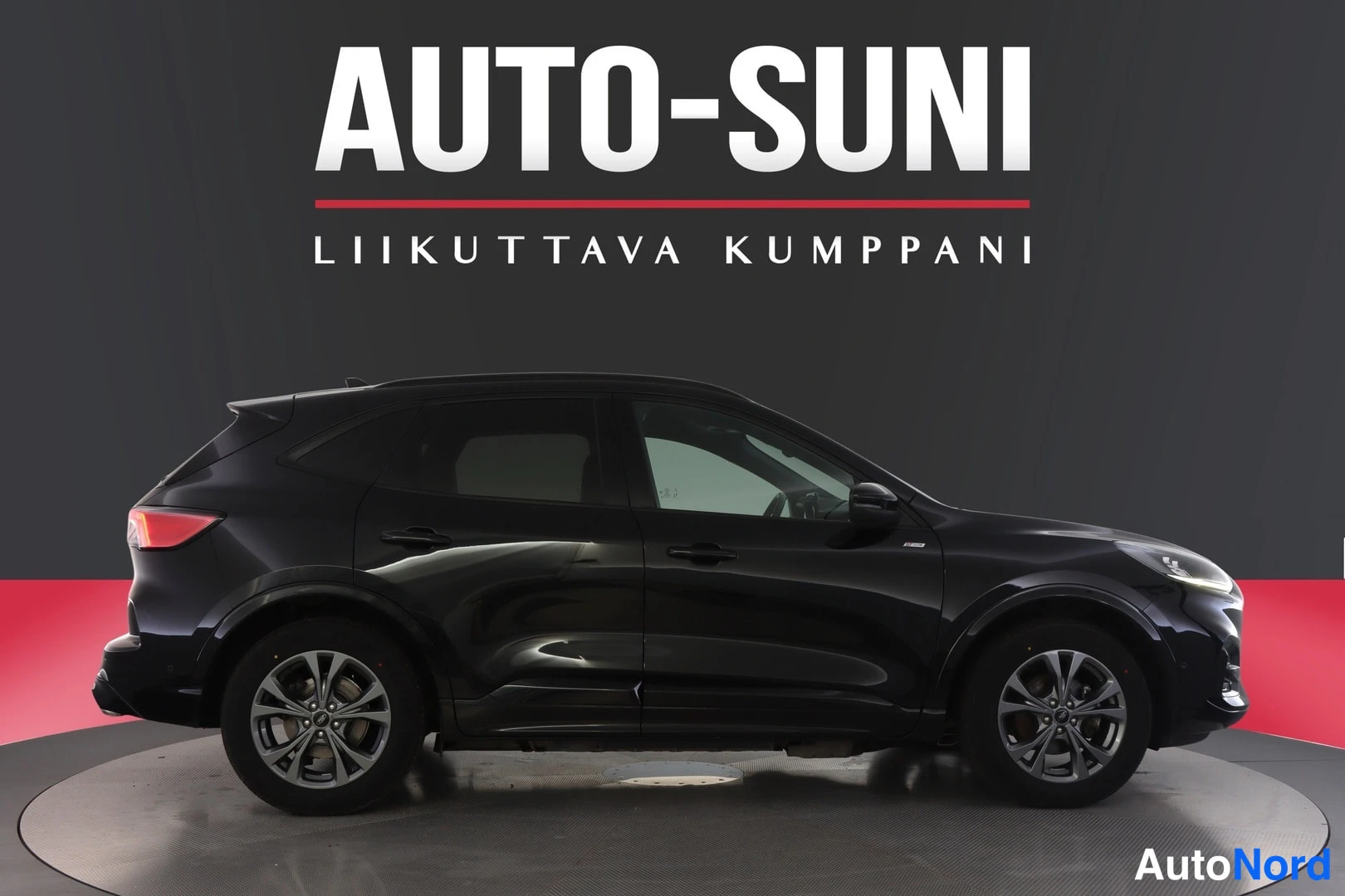 Sivulta: Musta Ford-auto vasemmalta kyljeltä. Kuvassa on koko auton profiili ja takavalot ovat päällä.