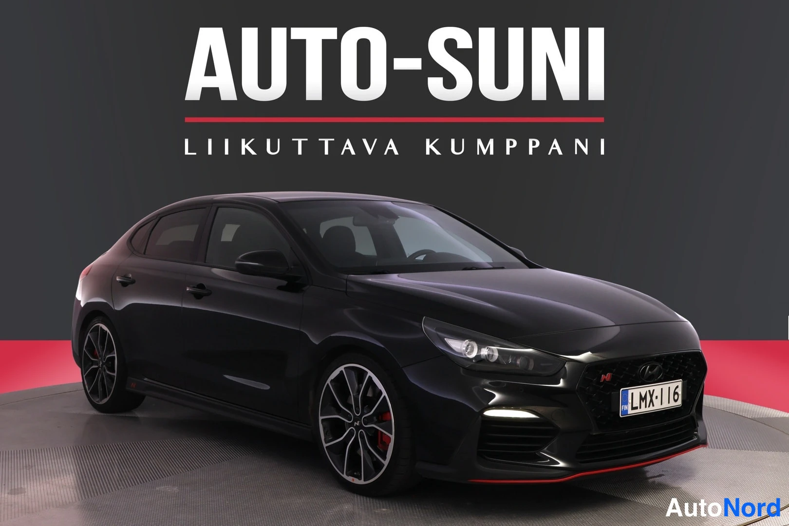 Etuviisto, nokka oikealle: Mustan hatchbackin etukulma. Etusäleikössä punainen N-merkki ja valkoinen rekisterikilpi.