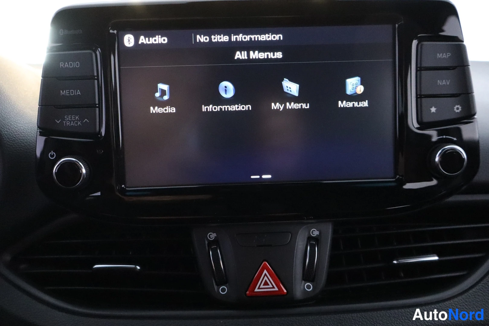 Etuviisto, nokka vasemmalle: Auton keskusnäyttö näyttää Audio-valikon: Media, Information, My Menu ja Manual; näytön yläkulmassa Bluetooth-merkintä.