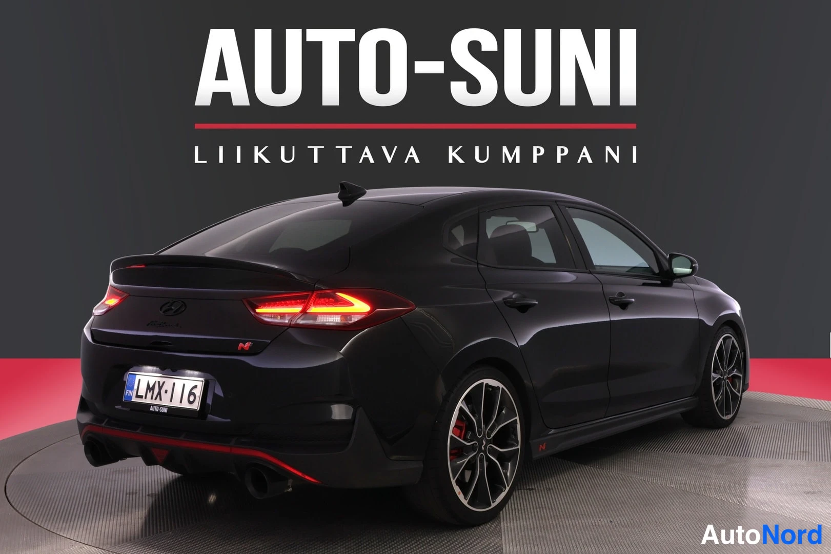 Takaviisto: Mustan hatchbackin takakulma vasemmalta. Taka­valot palavat ja peräosassa kaksi pakoputkea. Rekisterikilpi.