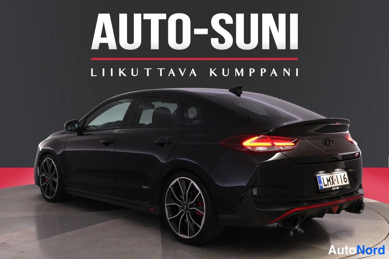 Takaviisto: Mustan hatchbackin takakulma oikealta. Takavalo palaa, perässä spoileri ja kaksi pakoputkea. Rekisterikilpi.