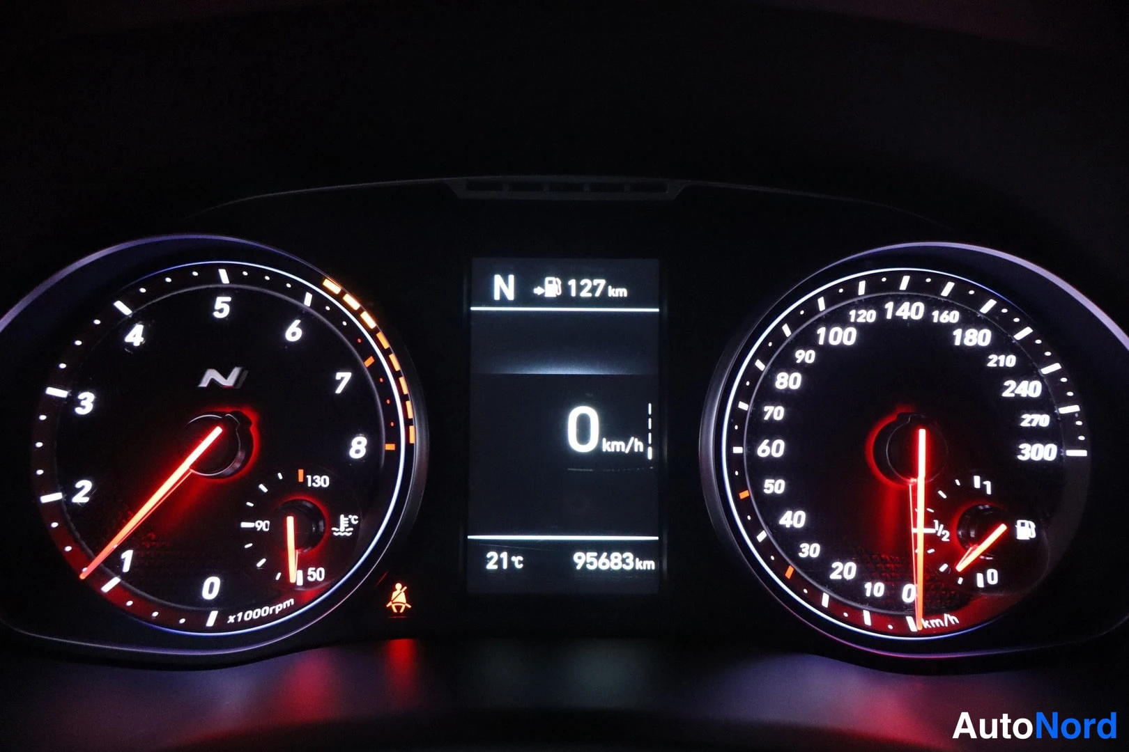 Yksityiskohta: Mittariston lähikuva pimeässä: kierroslukumittari asteikolla 8 x1000rpm, nopeusmittari asteikolla 300 km/h ja keskinäytössä N-merkki, 0 km/h, 127 km, 21 °C ja 9