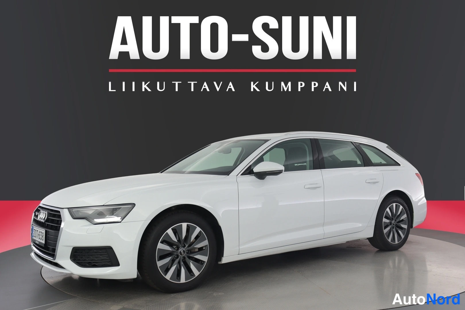 Etuviisto, nokka vasemmalle: Valkoinen farmarikorinen henkilöauto kulmakuvassa edestä vasemmalta; etusäleikkö, ajovalot ja auton vasen sivu näkyvät tummaa studio-taustaa vasten.