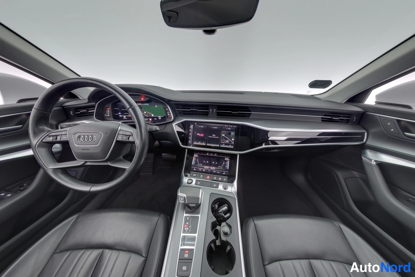 Yksityiskohta: Auton etuohjaamo keskeltä kuvattuna: Audi-ohjauspyörä, digitaalinen mittaristo, kaksi keskikonsolin näyttöä ja tummat etuistuimet.