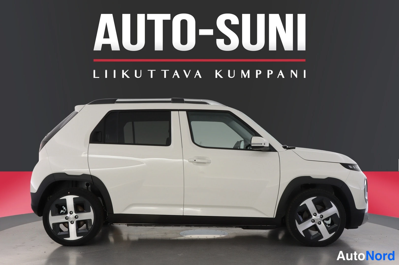Sivulta: The side view of the white car displays its profile, roof rails, and five-spoke alloy wheels against a studio background.