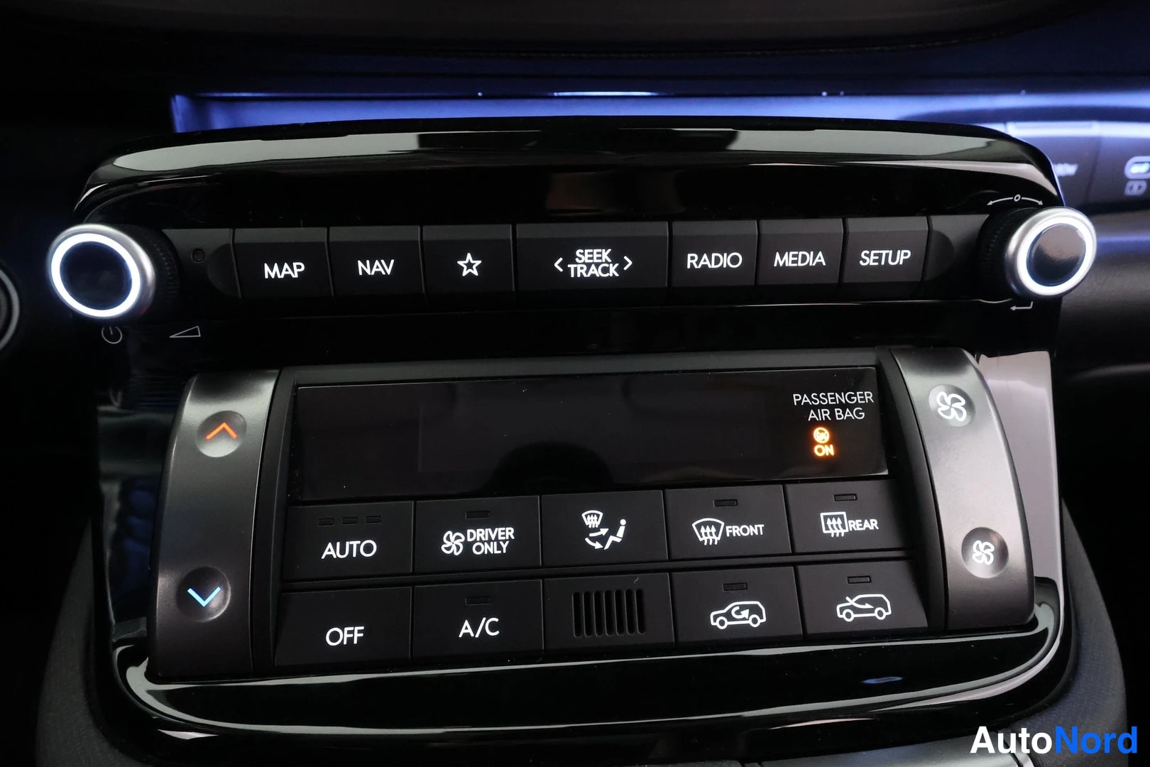 Yksityiskohta: Keskuskonsoli: painikerivi (MAP, NAV, SEEK TRACK, RADIO, MEDIA, SETUP) ja kaksivyöhykeilmastointi (AUTO, DRIVER ONLY, A/C, OFF, etu- ja takalasin sulatus); ilmo